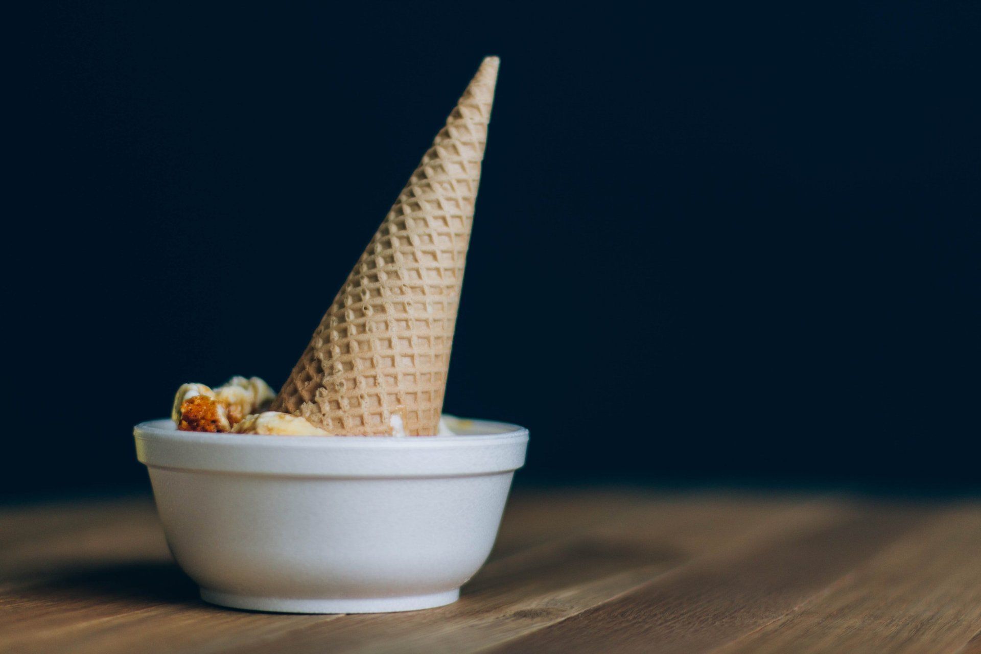 An ice cream cone is sitting in a bowl on a wooden table.