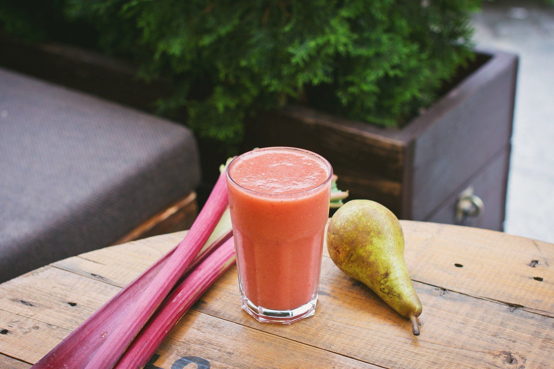 A glass of juice is sitting on a wooden table next to a pear and rhubarb.