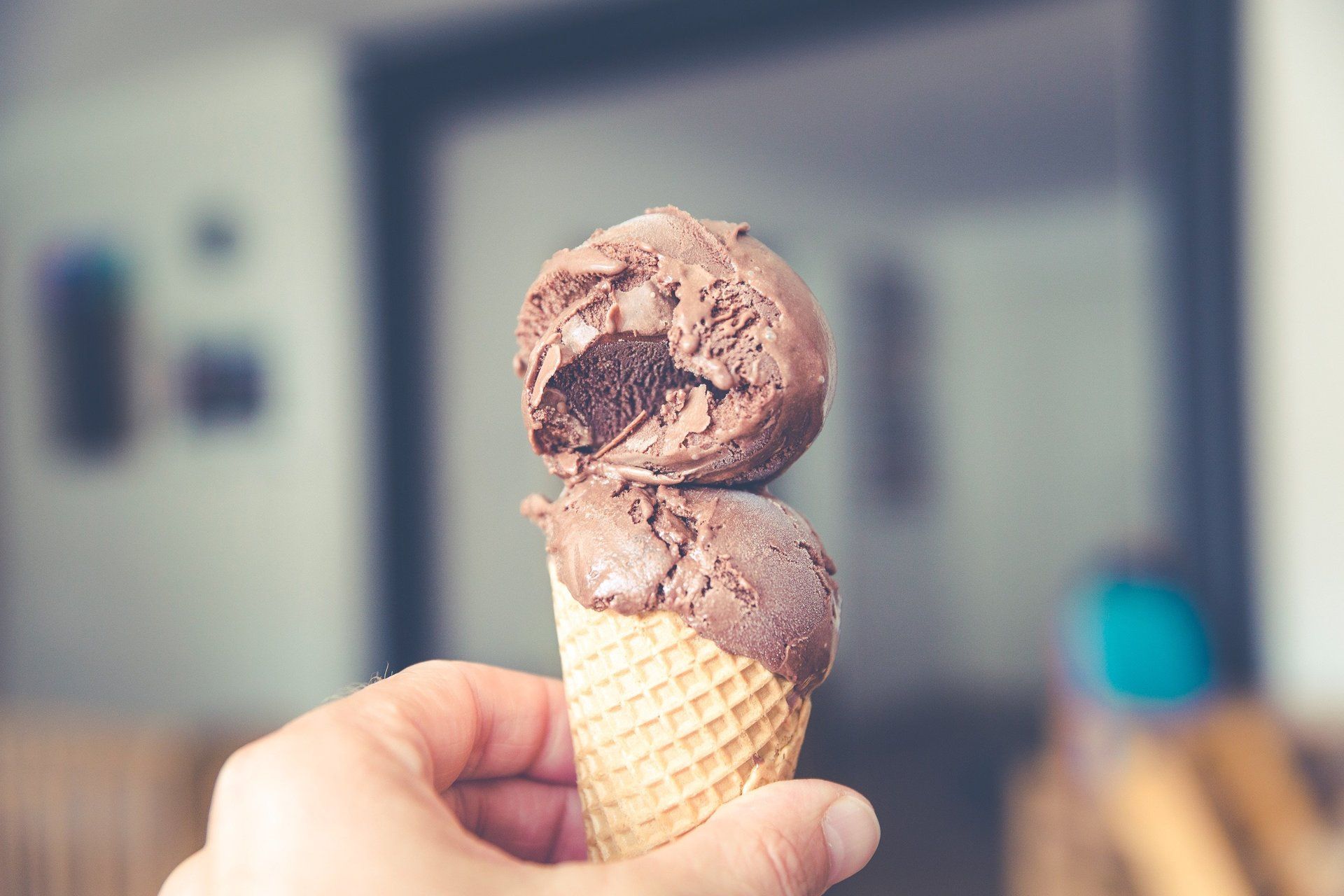A person is holding two scoops of chocolate ice cream in a waffle cone.