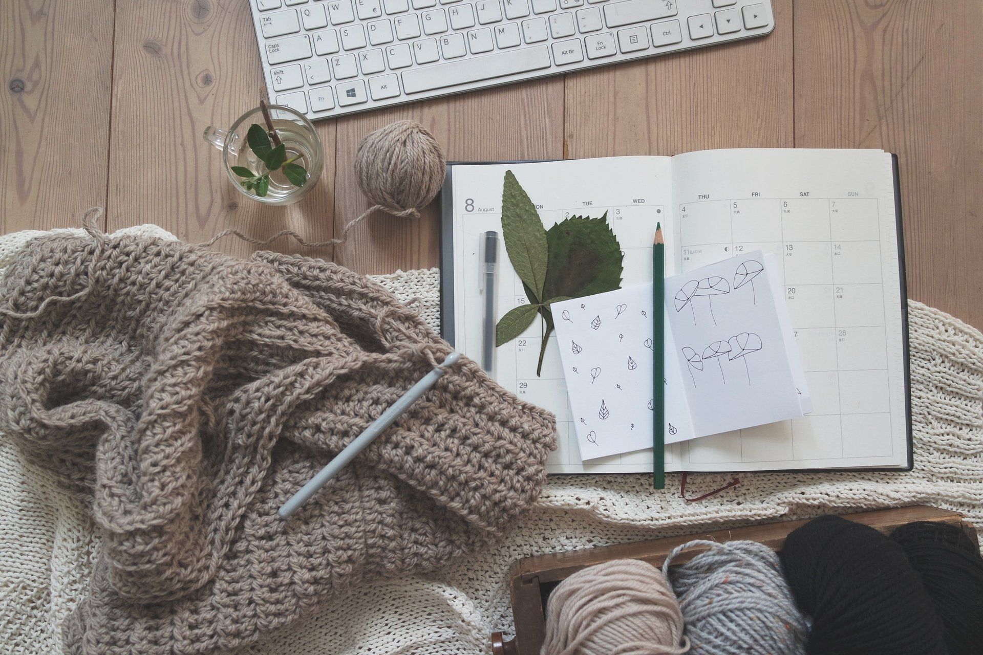 GK Marketing Online | A knitted scarf , yarn , pencils , a notebook and a keyboard are on a wooden table.