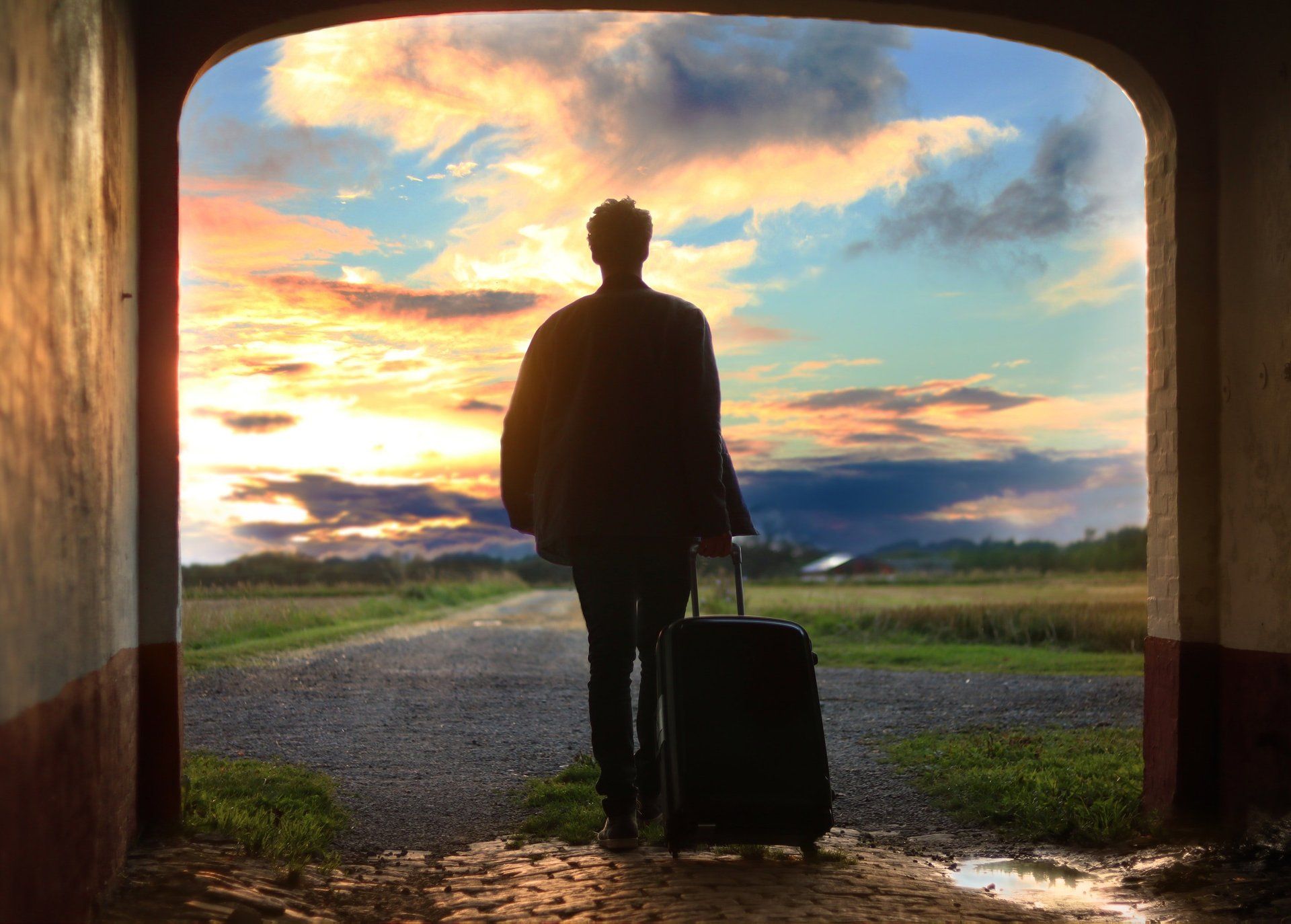 woman with suitcase in doorway looking out onto a wide open space with a colorful sunset