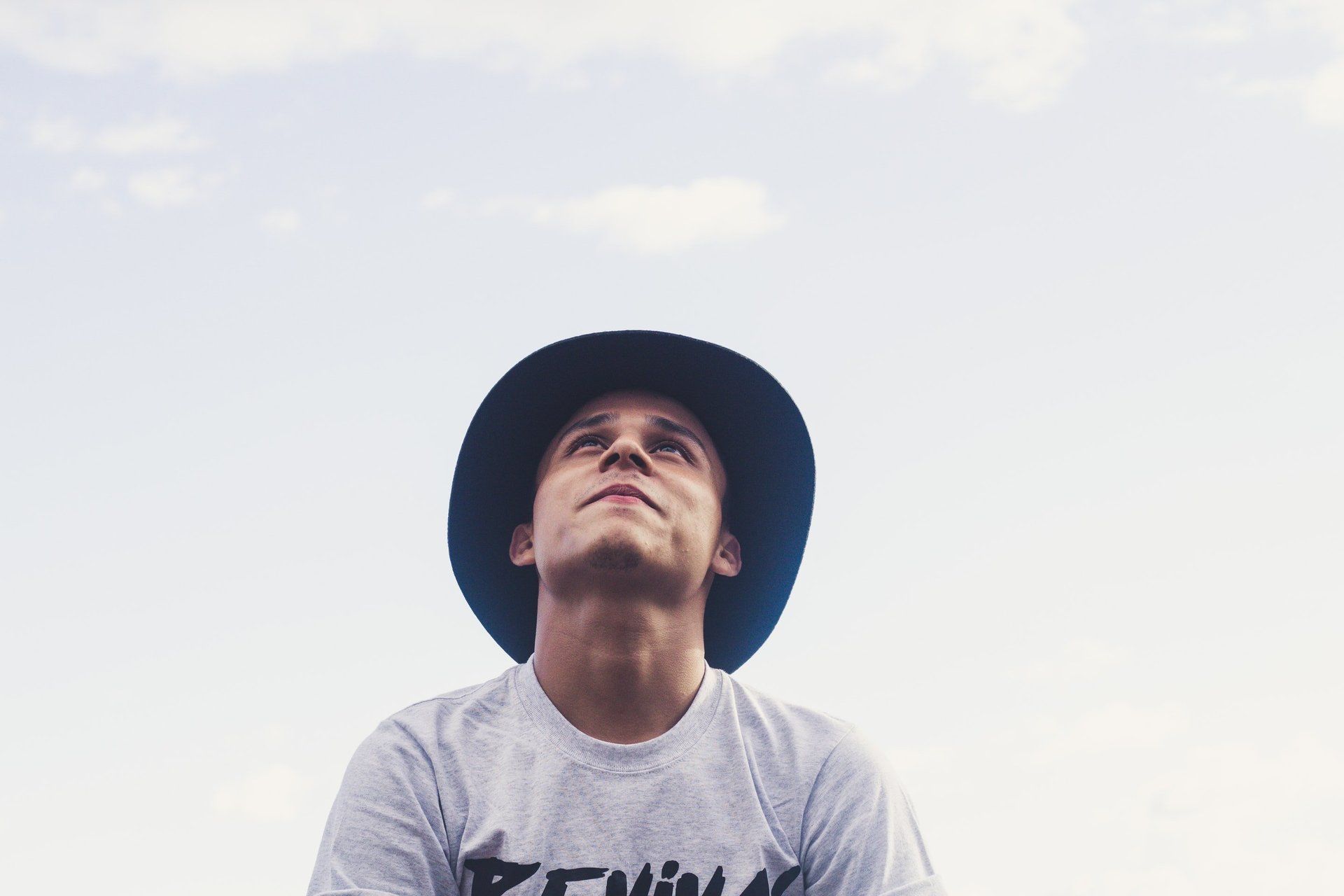 A man wearing a hat and a t-shirt is looking up at the sky.