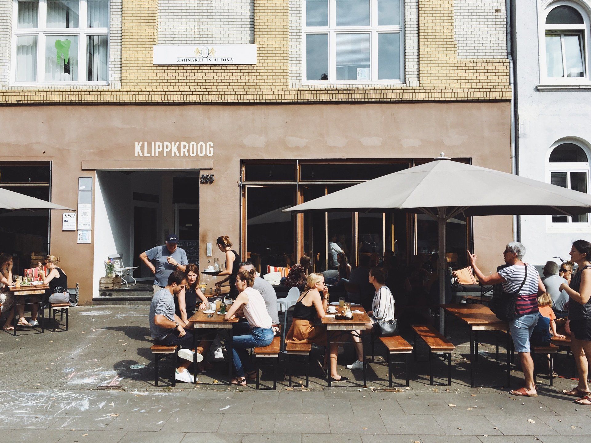 A group of people are sitting at tables outside of a restaurant with umbrellas.