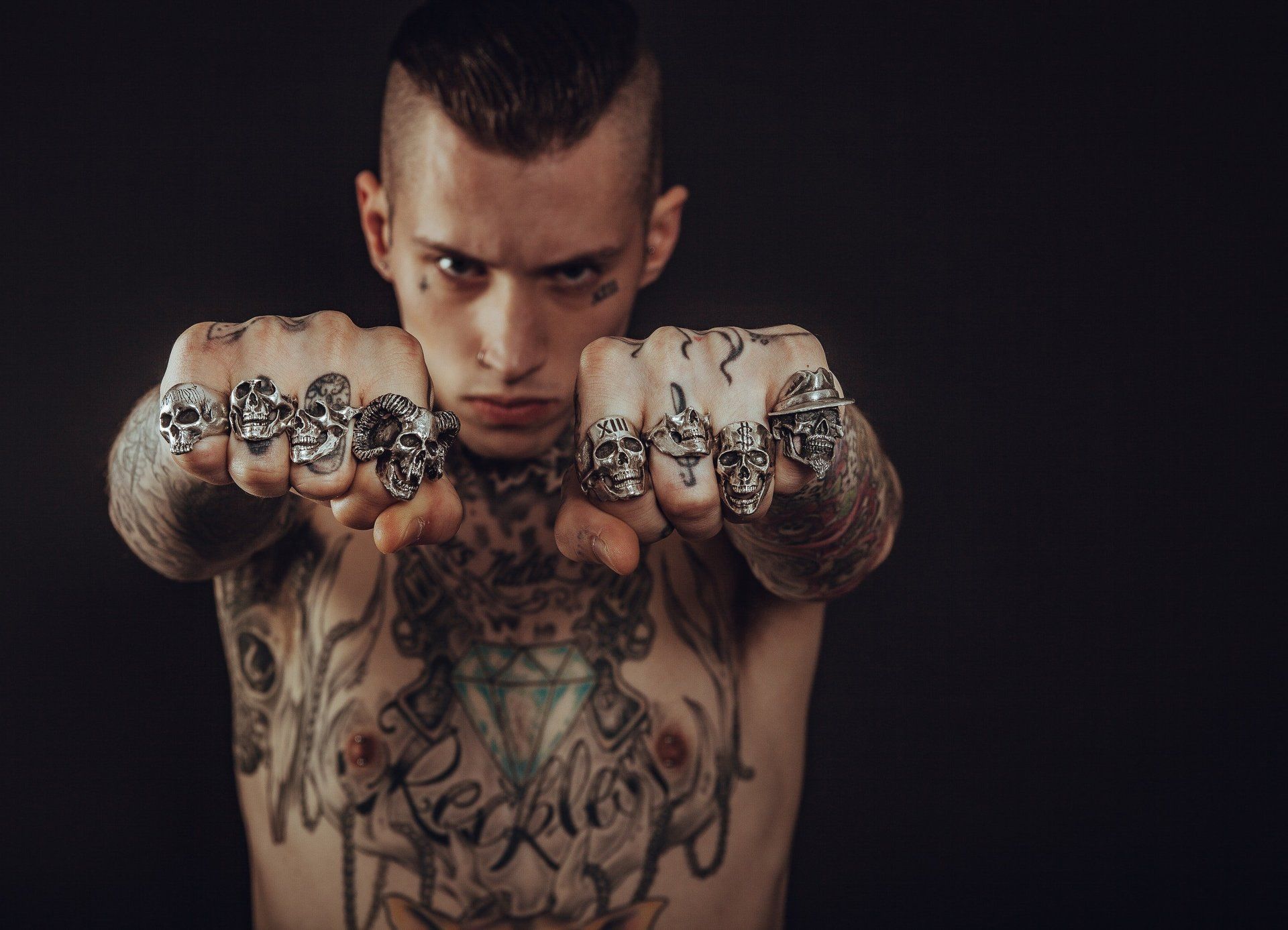A shirtless tattooed man is holding up his rings