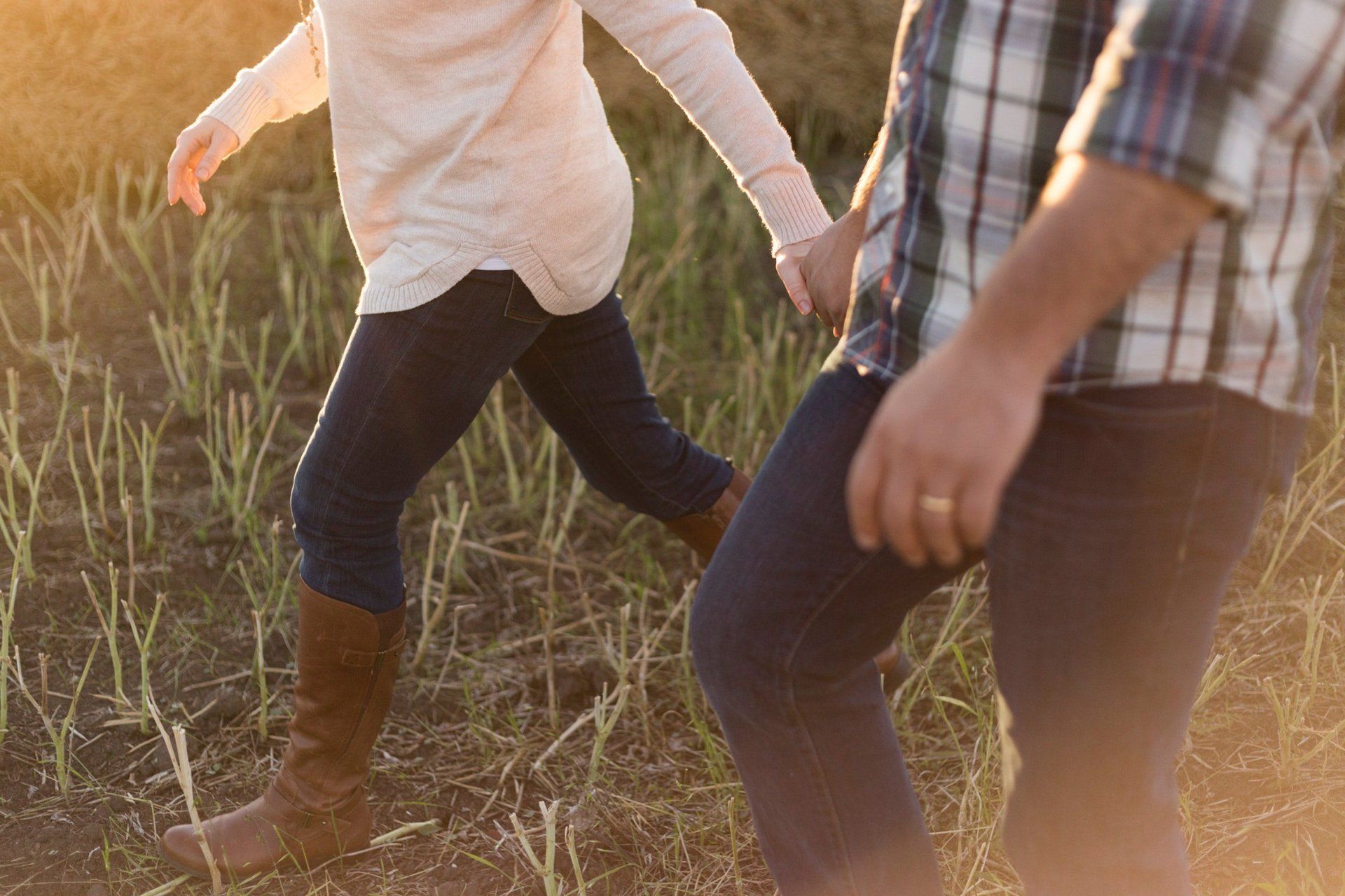 Couple walking hand-in-hand through tall grass, bathed in warm sunlight.