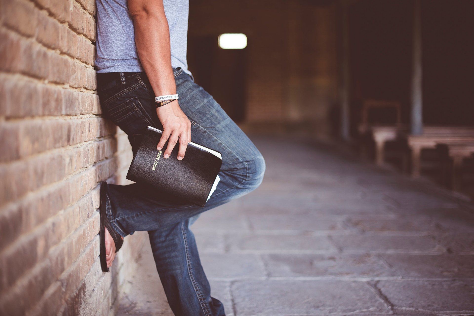 Young man holding Bible, leaning against wall