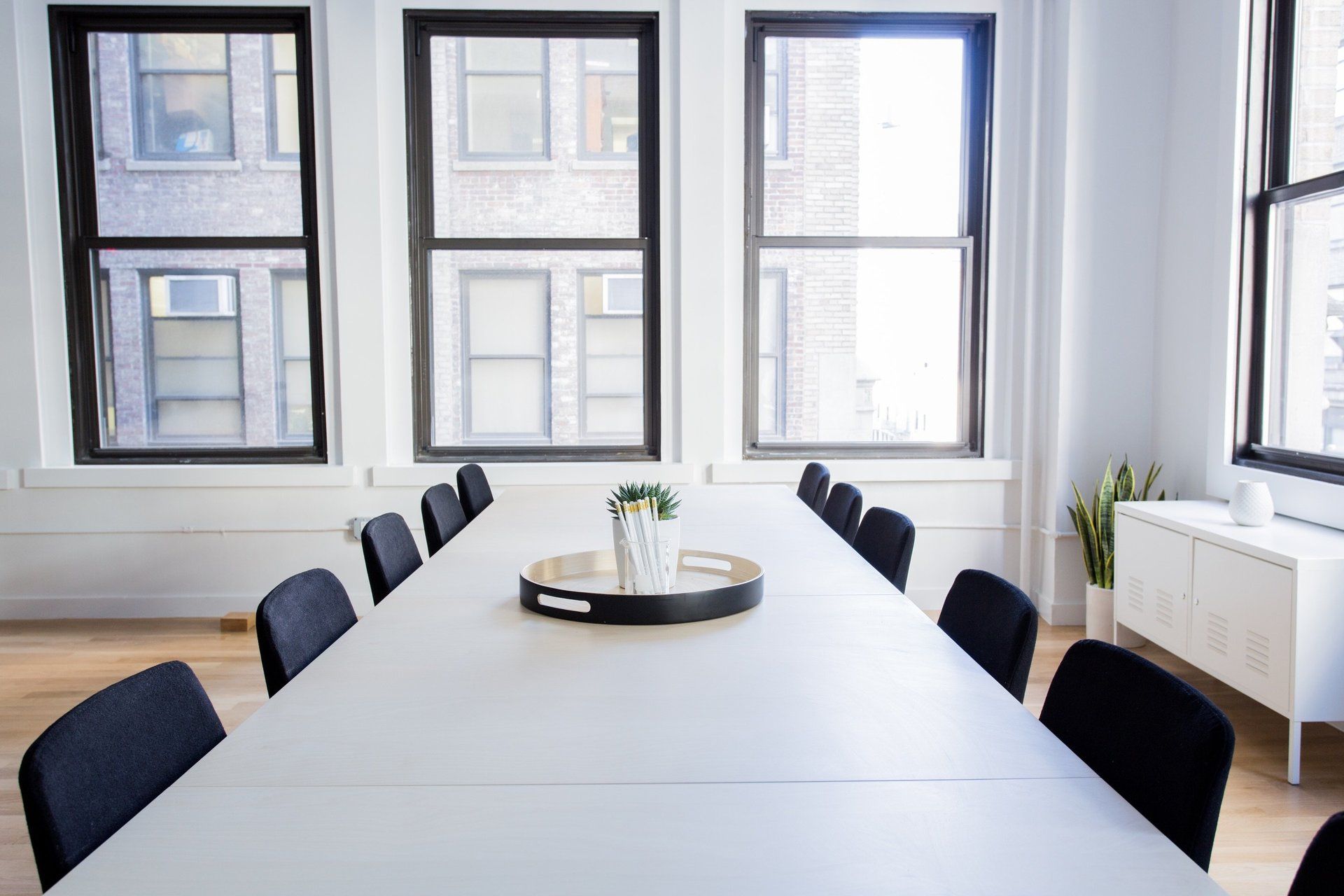 A conference room with a long white table and black chairs.