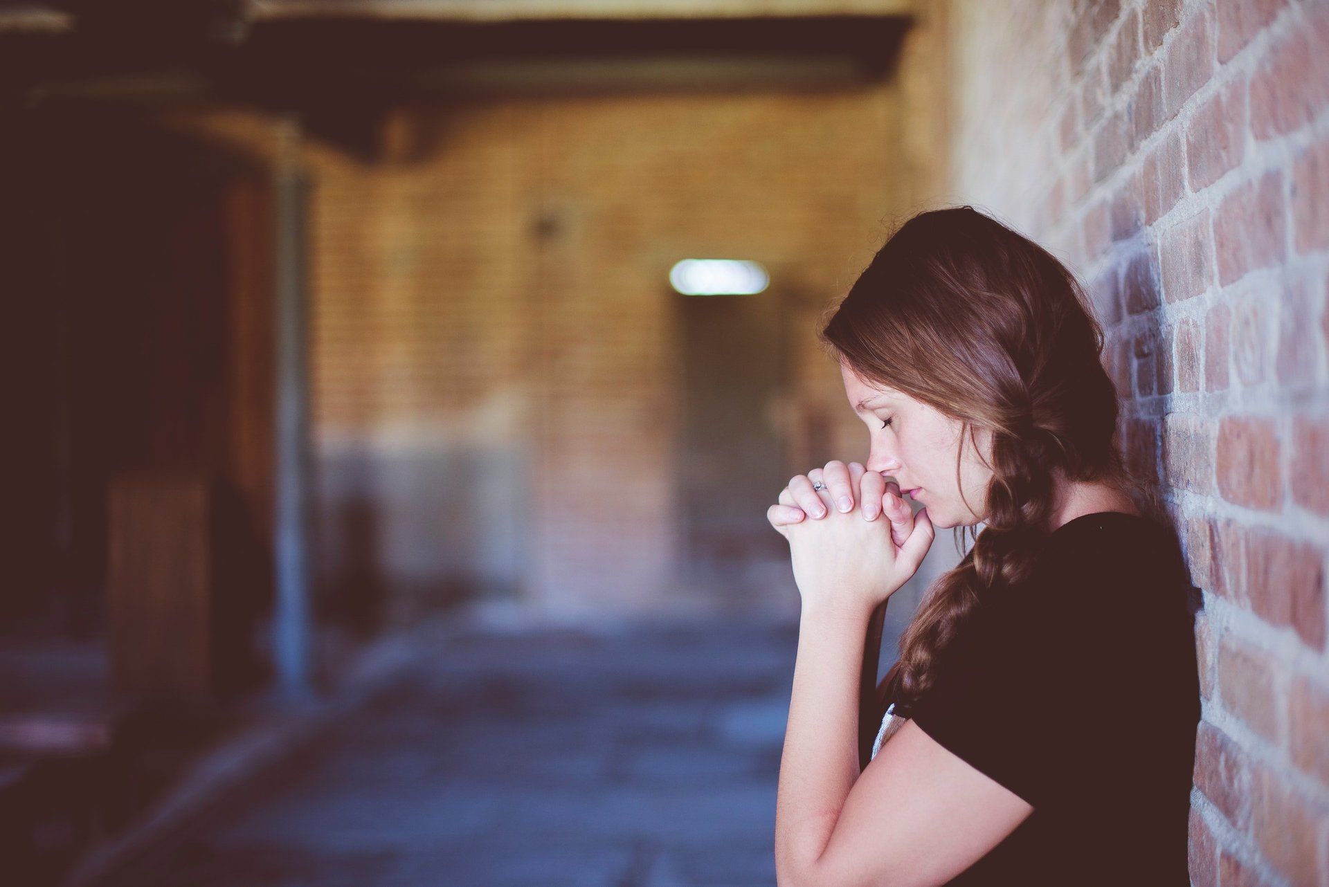 Young woman with back to wall, praying