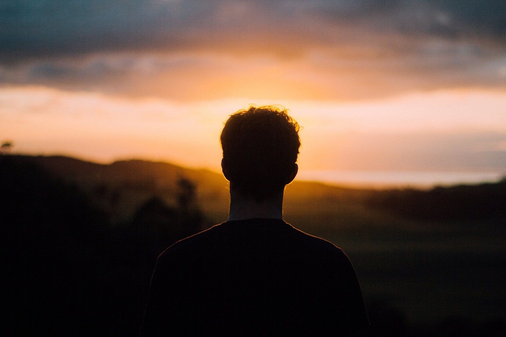 A man is standing in front of a sunset in a field.