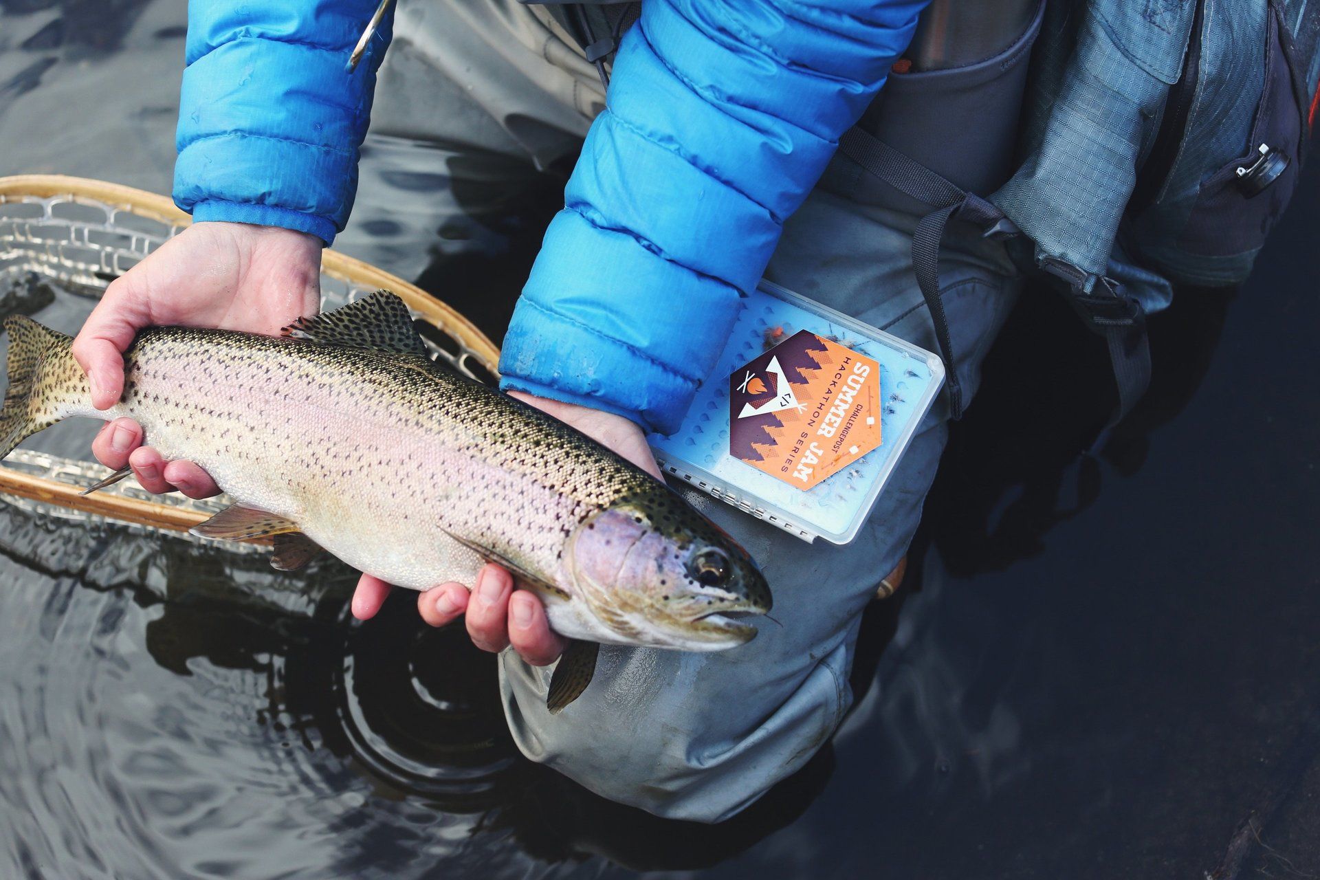 a person holding a rainbow trout next to a fly box that says fly fishing