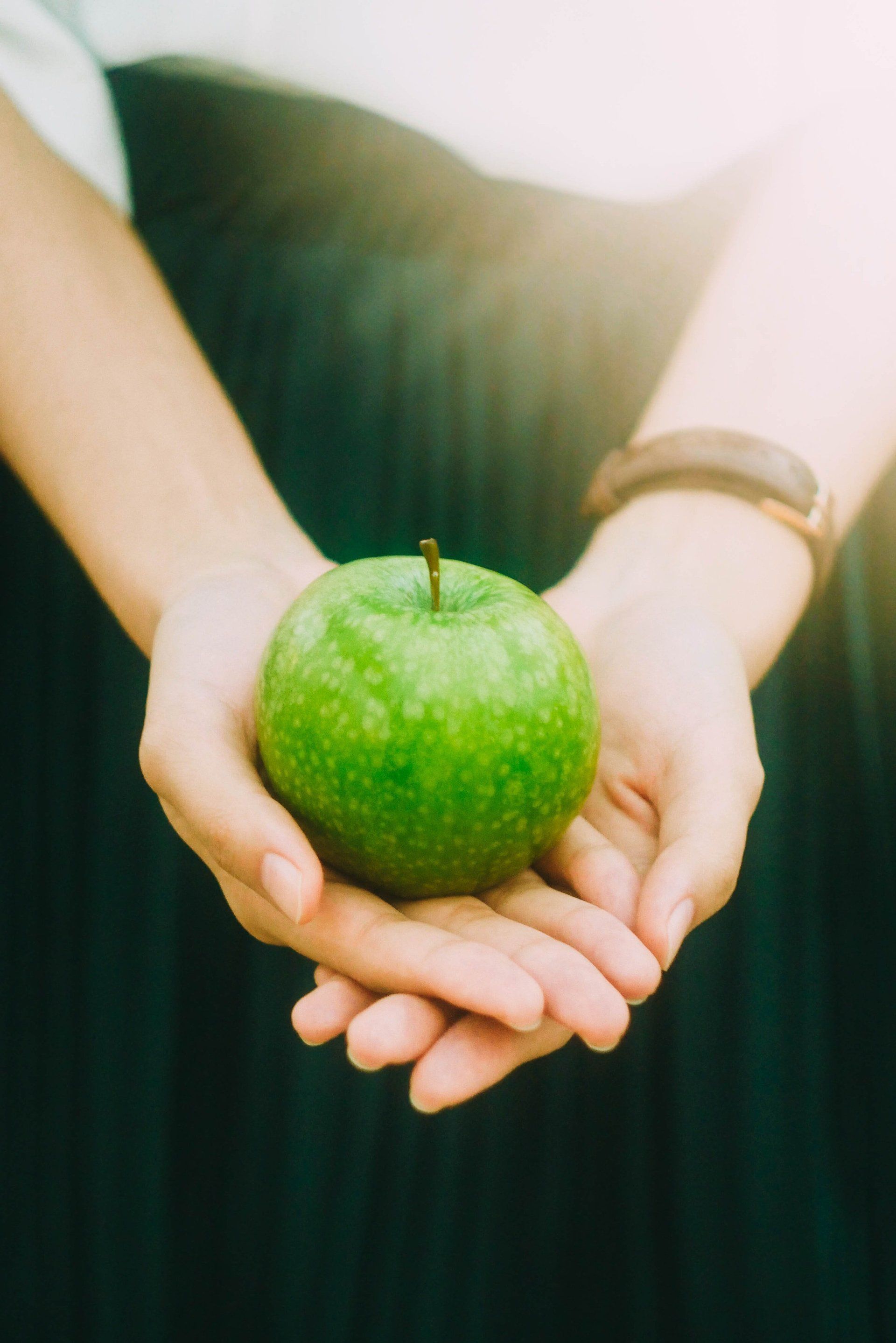 Two hands holding out a green apple