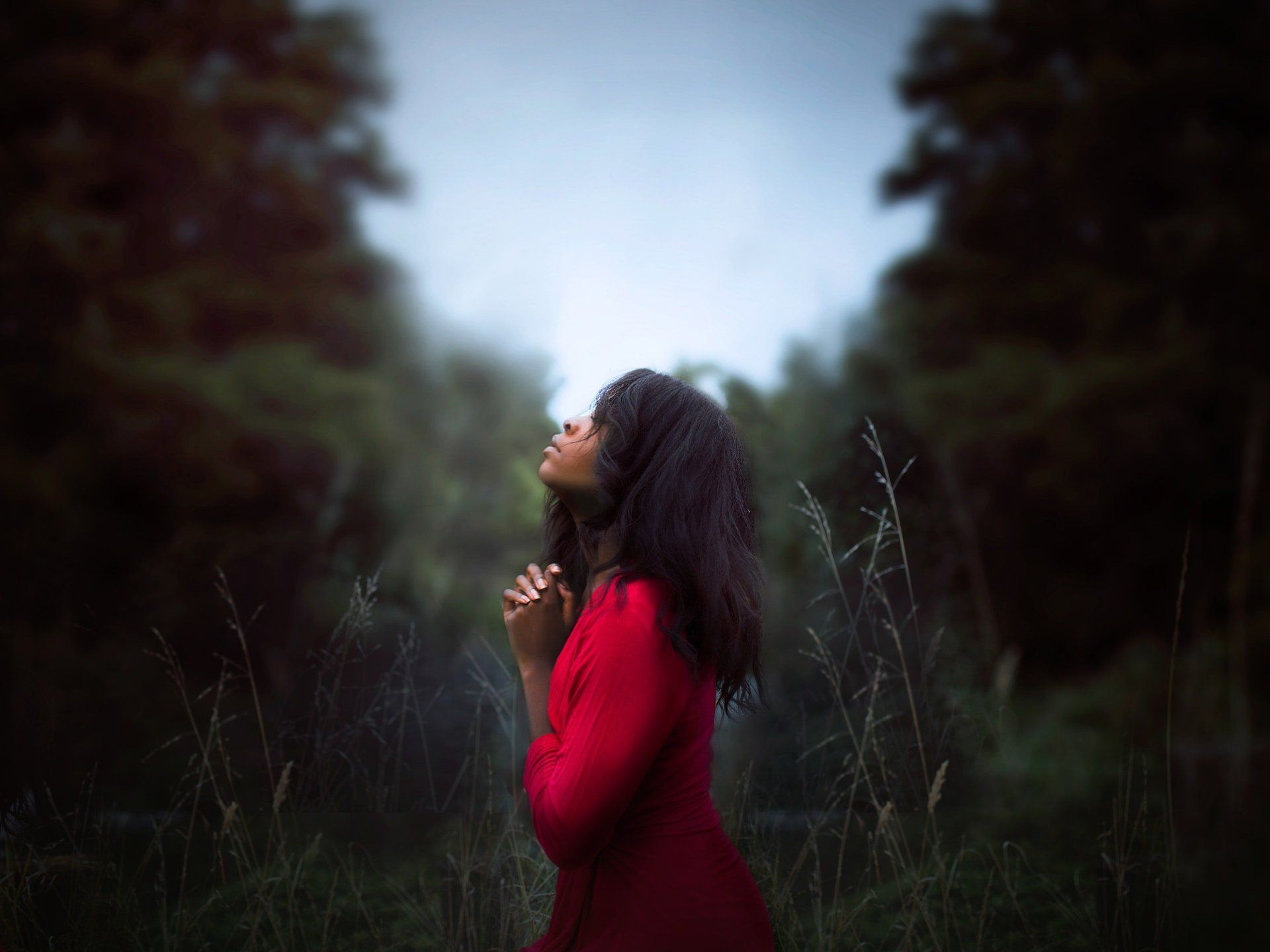 young woman praying in a field with trees looking up to the sky