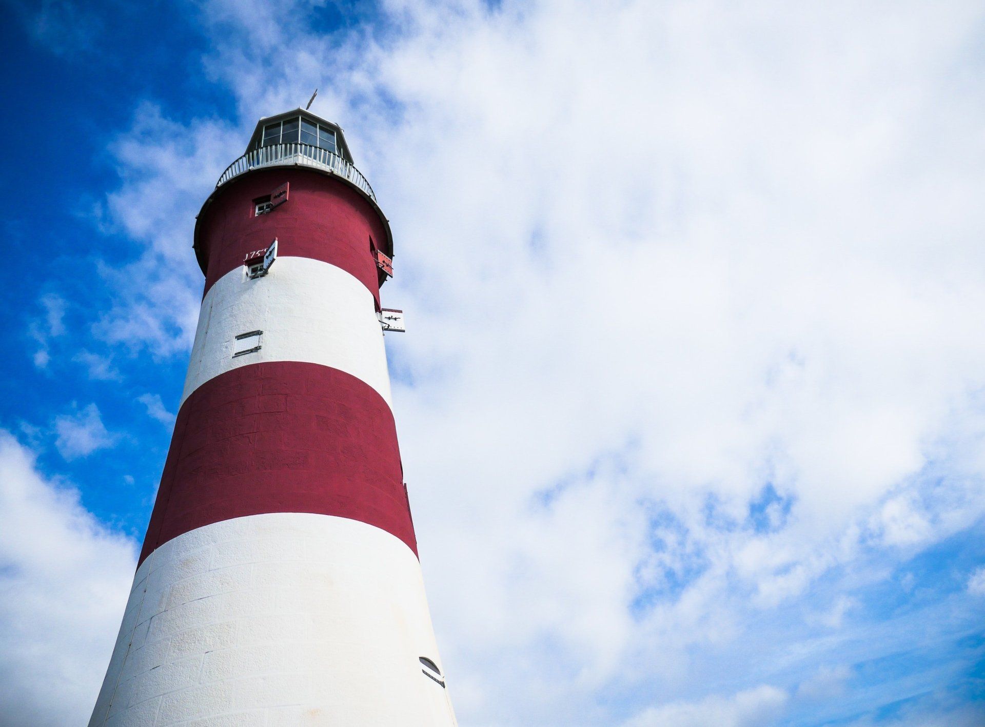 A red and white lighthouse against a blue sky with clouds