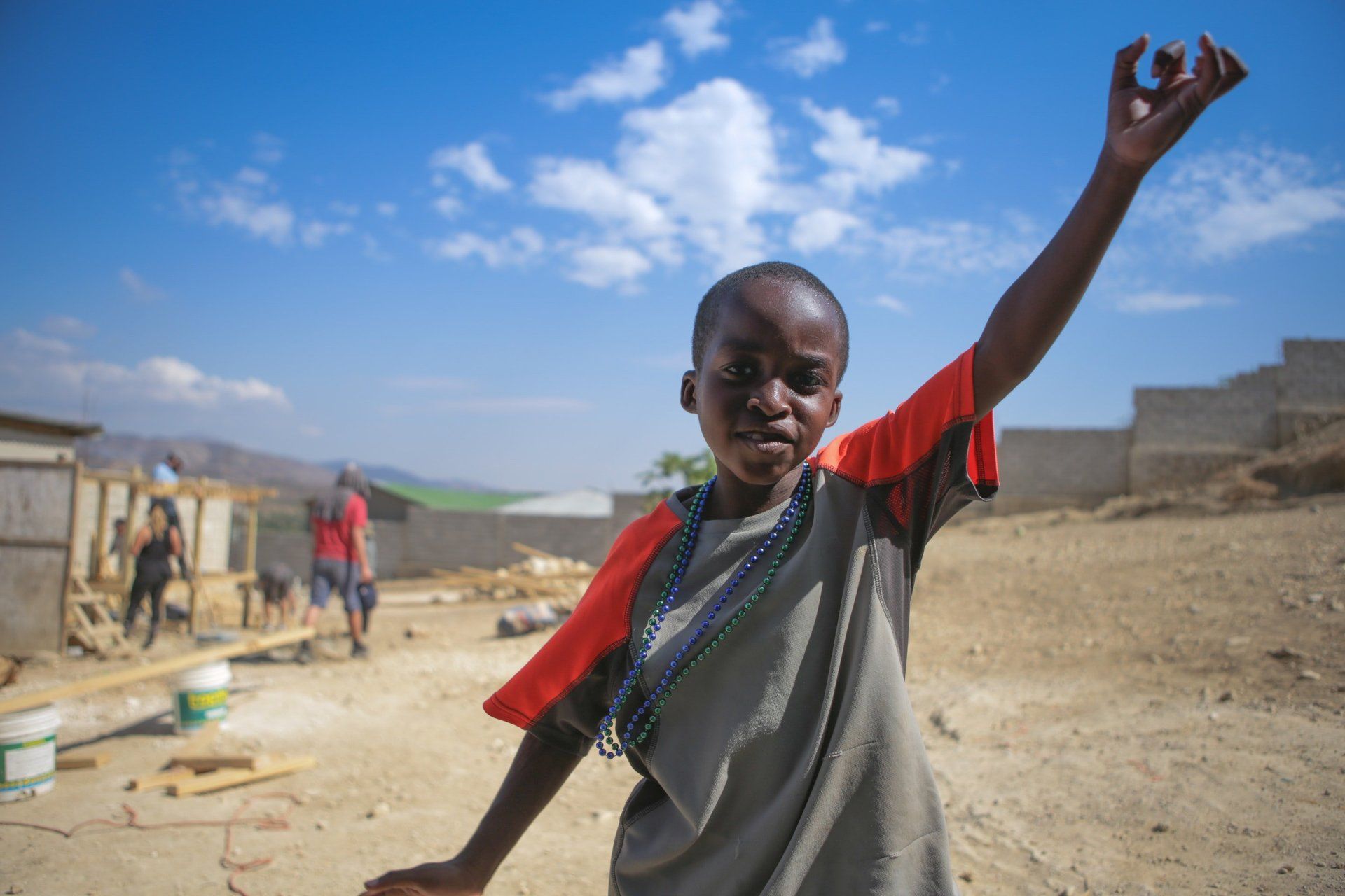 A young boy is standing in a dirt field with his arm in the air.