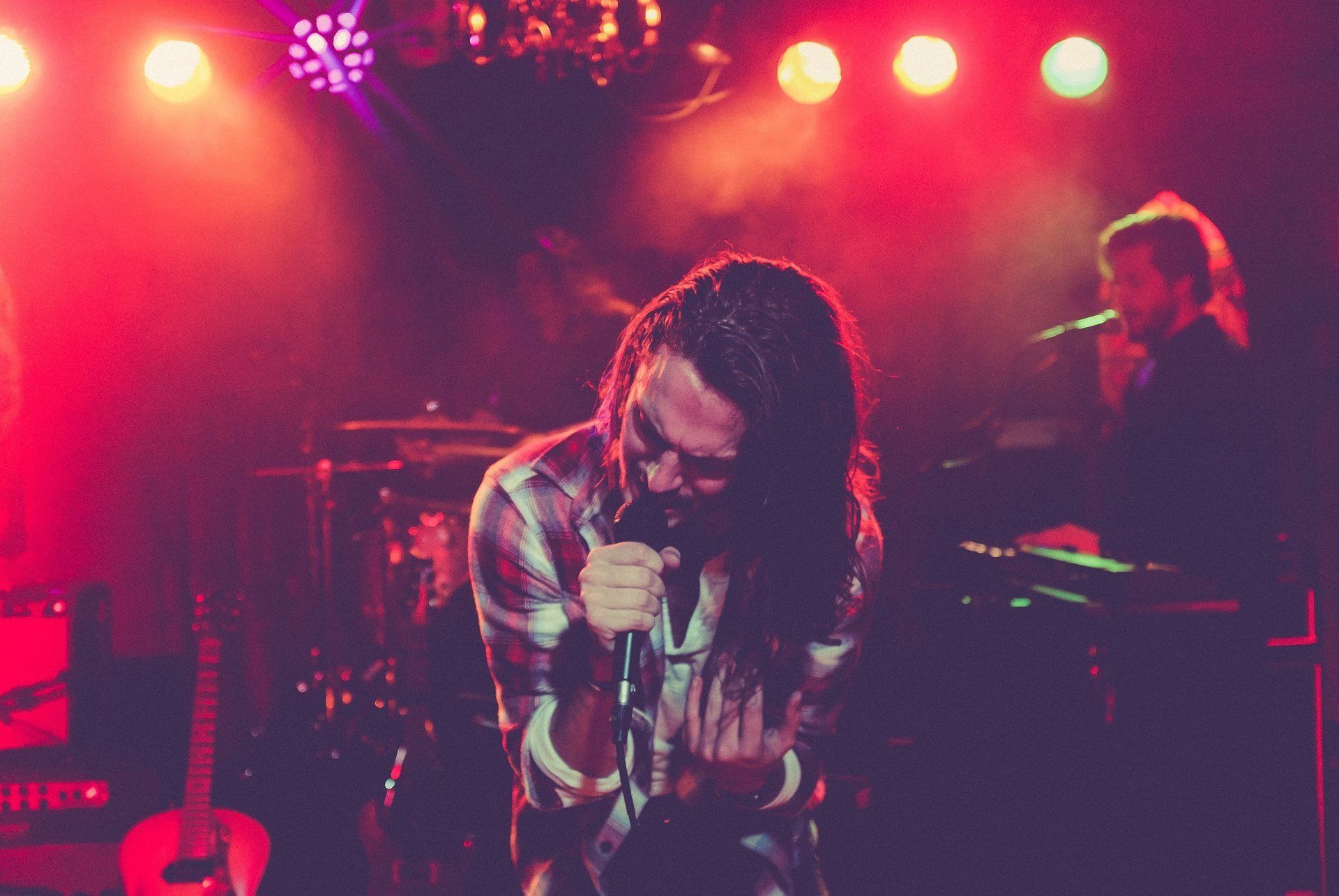A man with long hair is singing into a microphone on a stage.