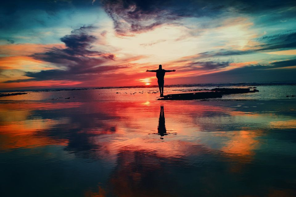 person standing near water at sunset with arms out