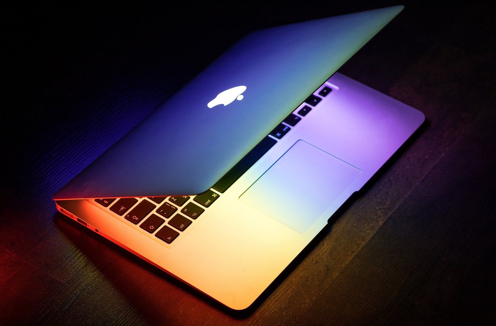 A rainbow colored apple laptop is open on a table