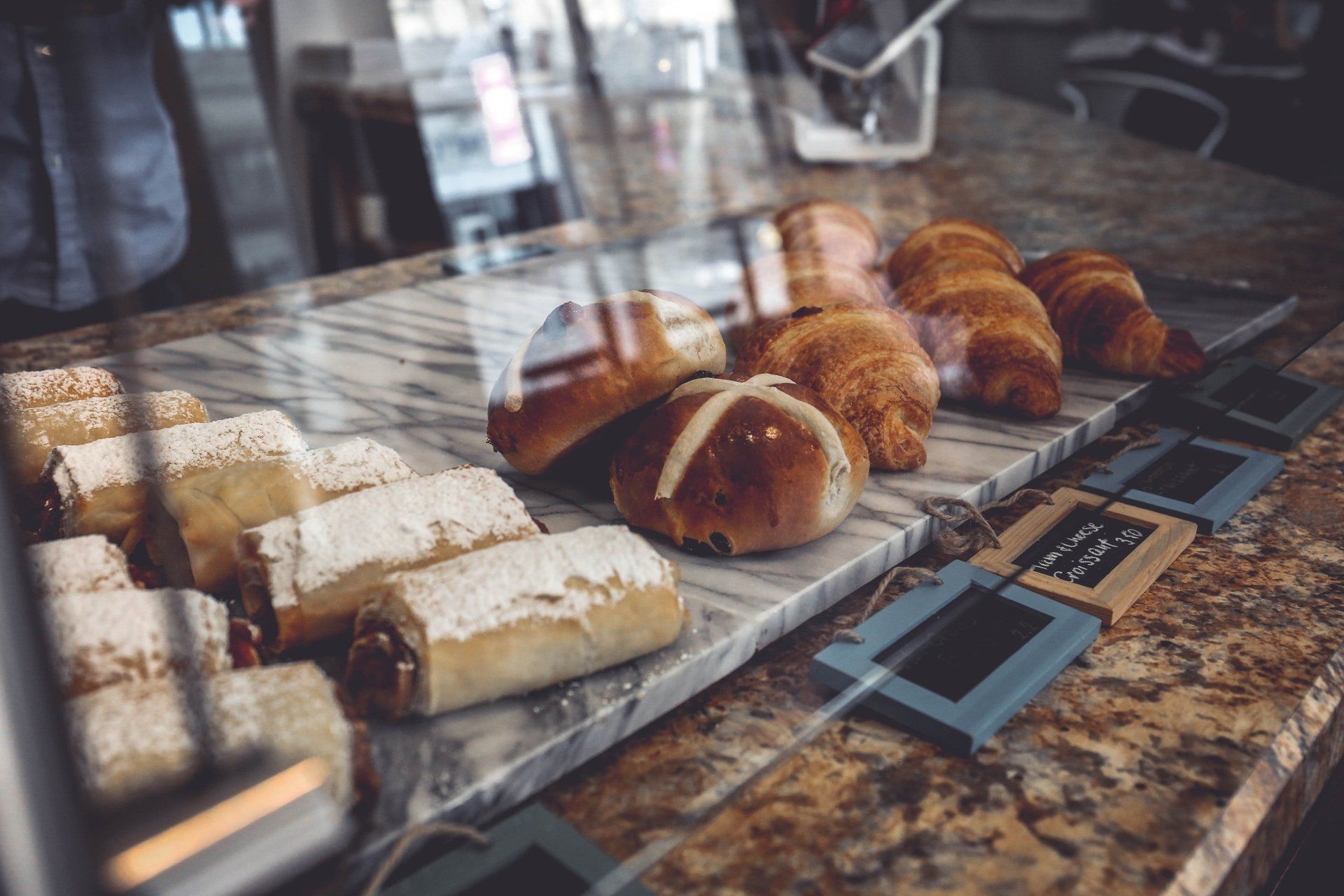 Pastries displayed inside a bakery showcase: croissants, rolls, and dusted rectangular pastries.