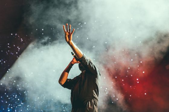 Image of a man standing on the stage, he's holing a microphone and there is a smoke effect behind him
