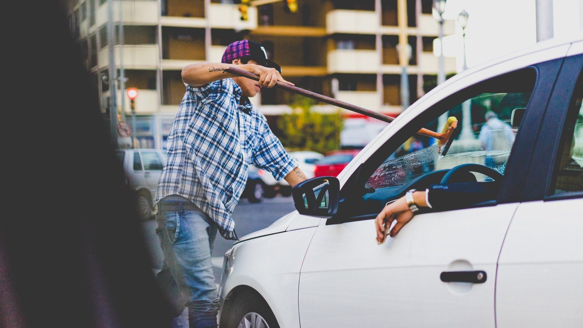 A man is standing next to a white car with a stick in his hand.