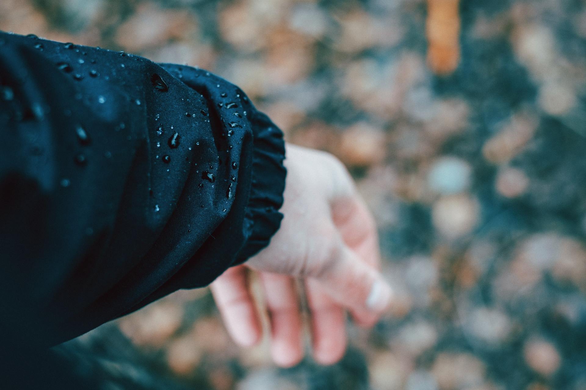 A person wearing a black jacket with water drops on it.