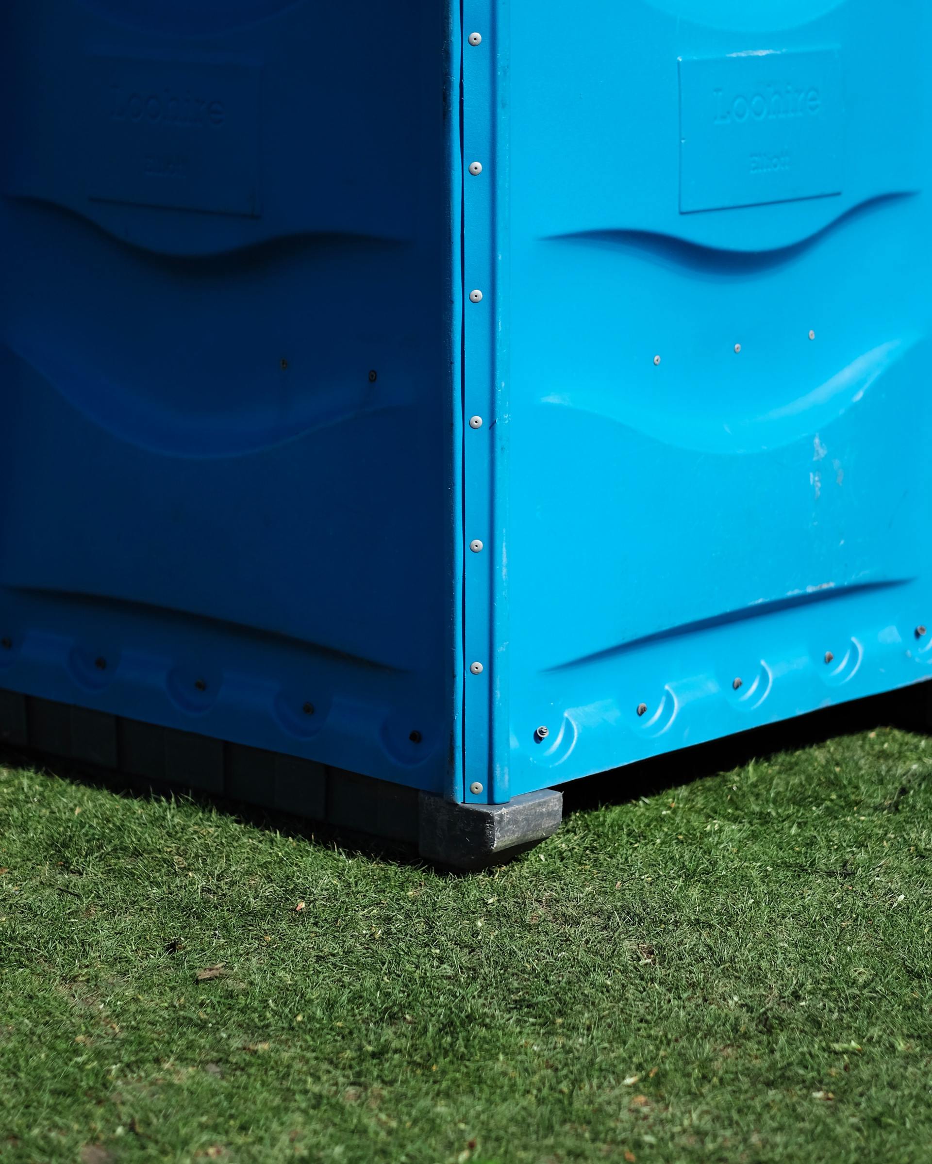A Blue Portable Toilet Is Sitting On Top Of A Lush Green Field — Grafton Hire In South Grafton, NSW