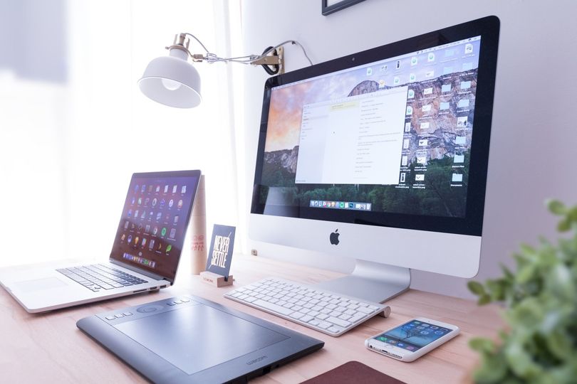 Desk with computer, laptop, tablet, and phone; lamp and plant.
