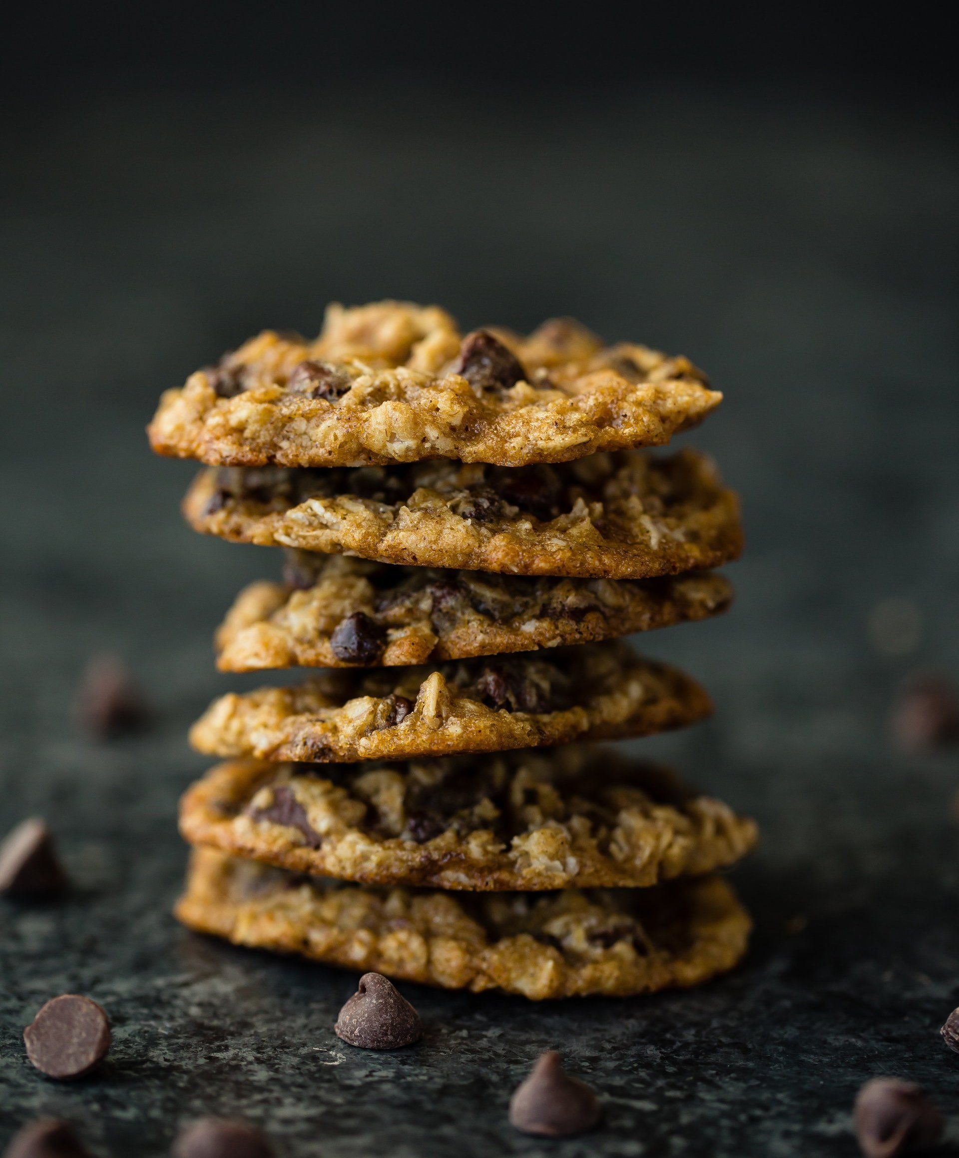 Stack of five oatmeal chocolate chip cookies on a dark surface, with scattered chocolate chips.