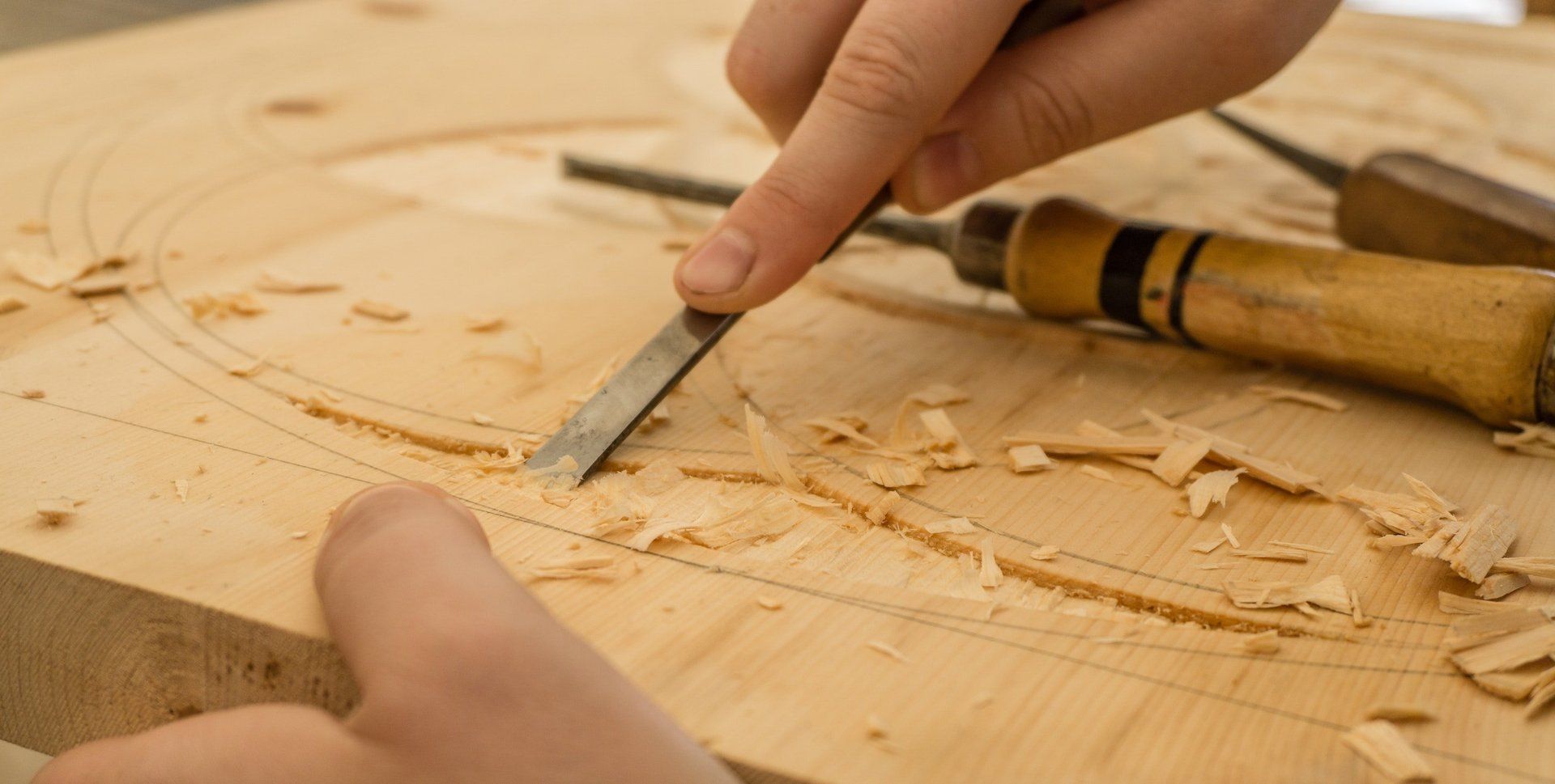 Hands carving into wood with woodworking tools 
