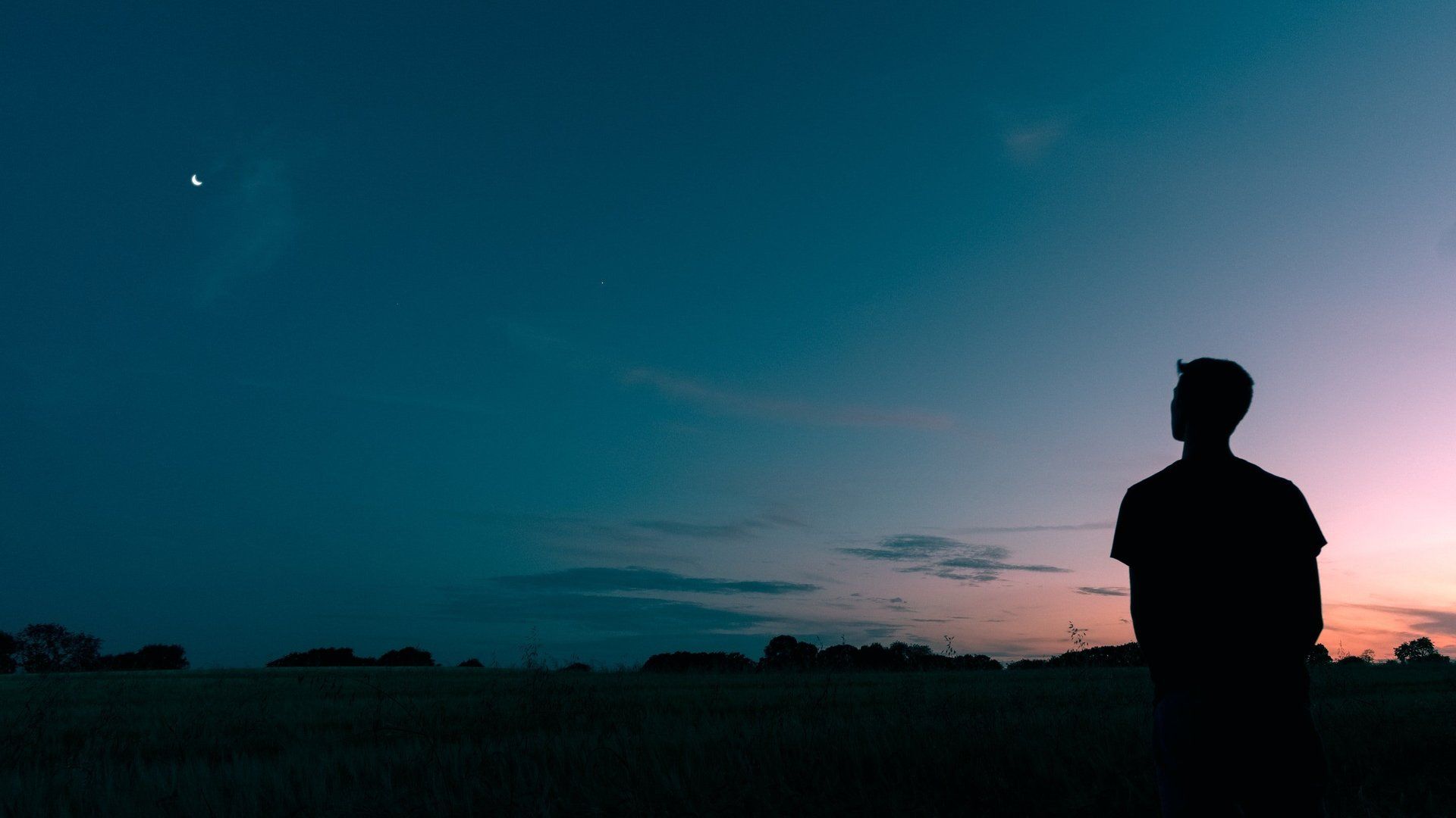 A silhouette of a man standing in a field at sunset.