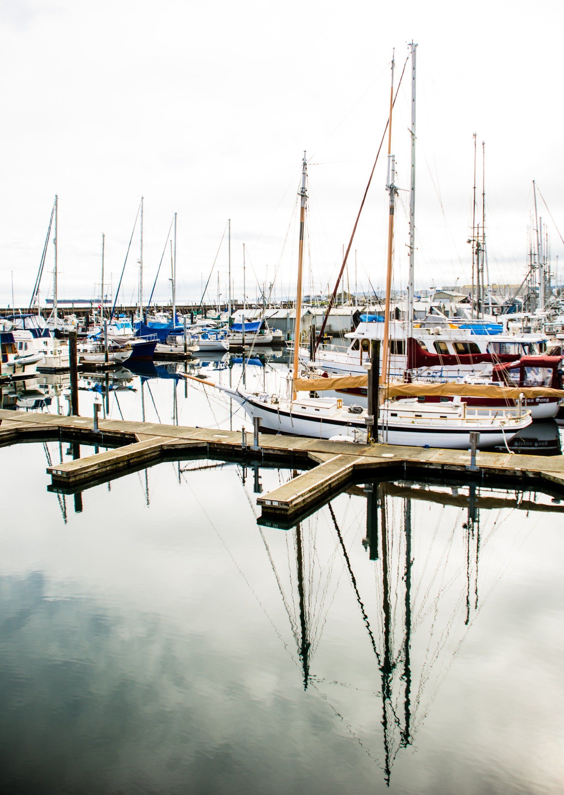 A row of boats are docked at a marina on a cloudy day