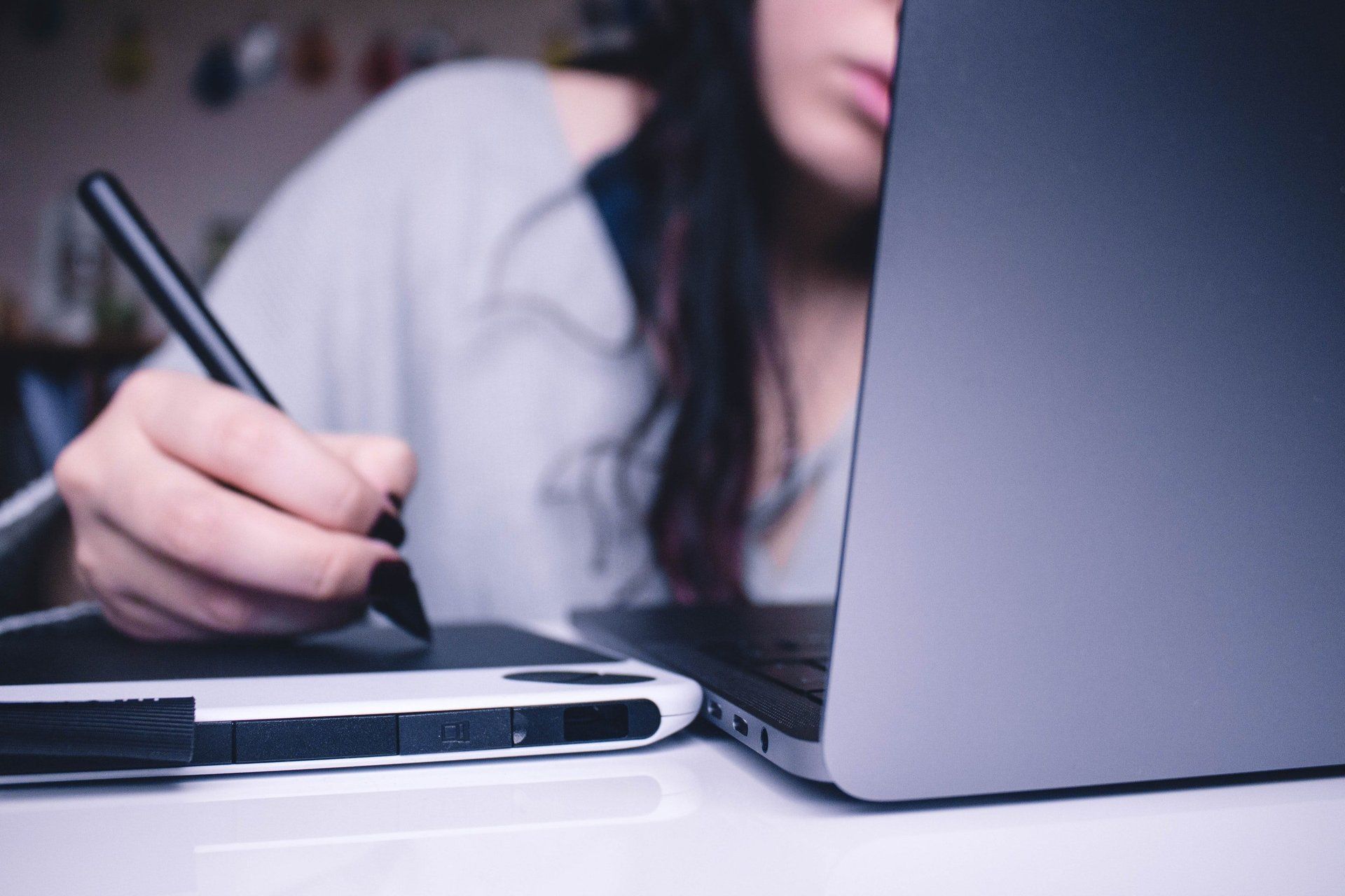 Una donna usa una penna per disegnare su un tablet accanto a un laptop.