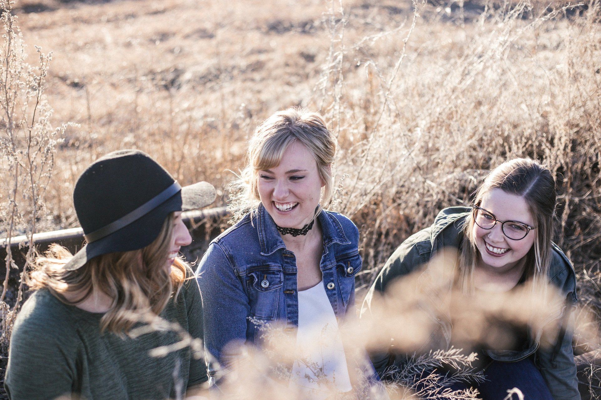 Three women are sitting in a field talking to each other.