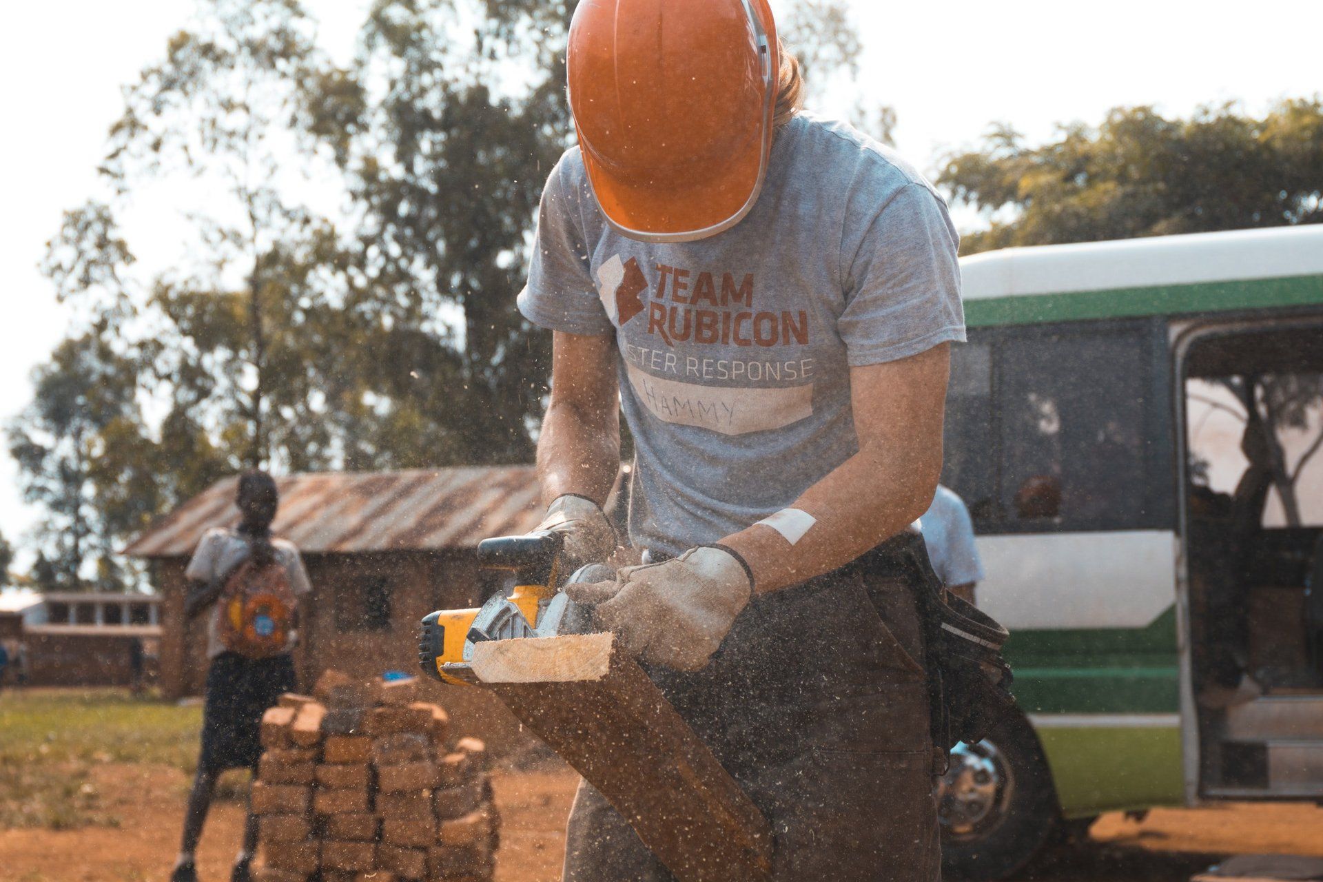 A man wearing a team rubicon shirt is cutting a piece of wood