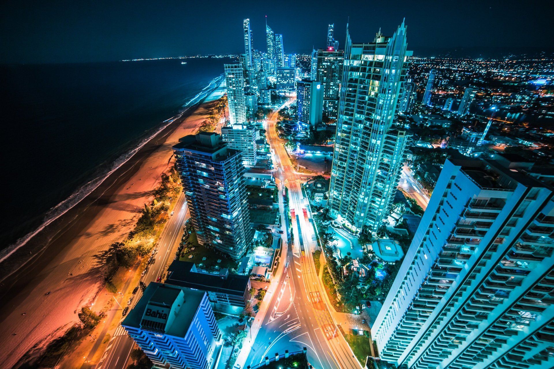 City skyline at night, buildings lit up with blue and white lights along the coast.