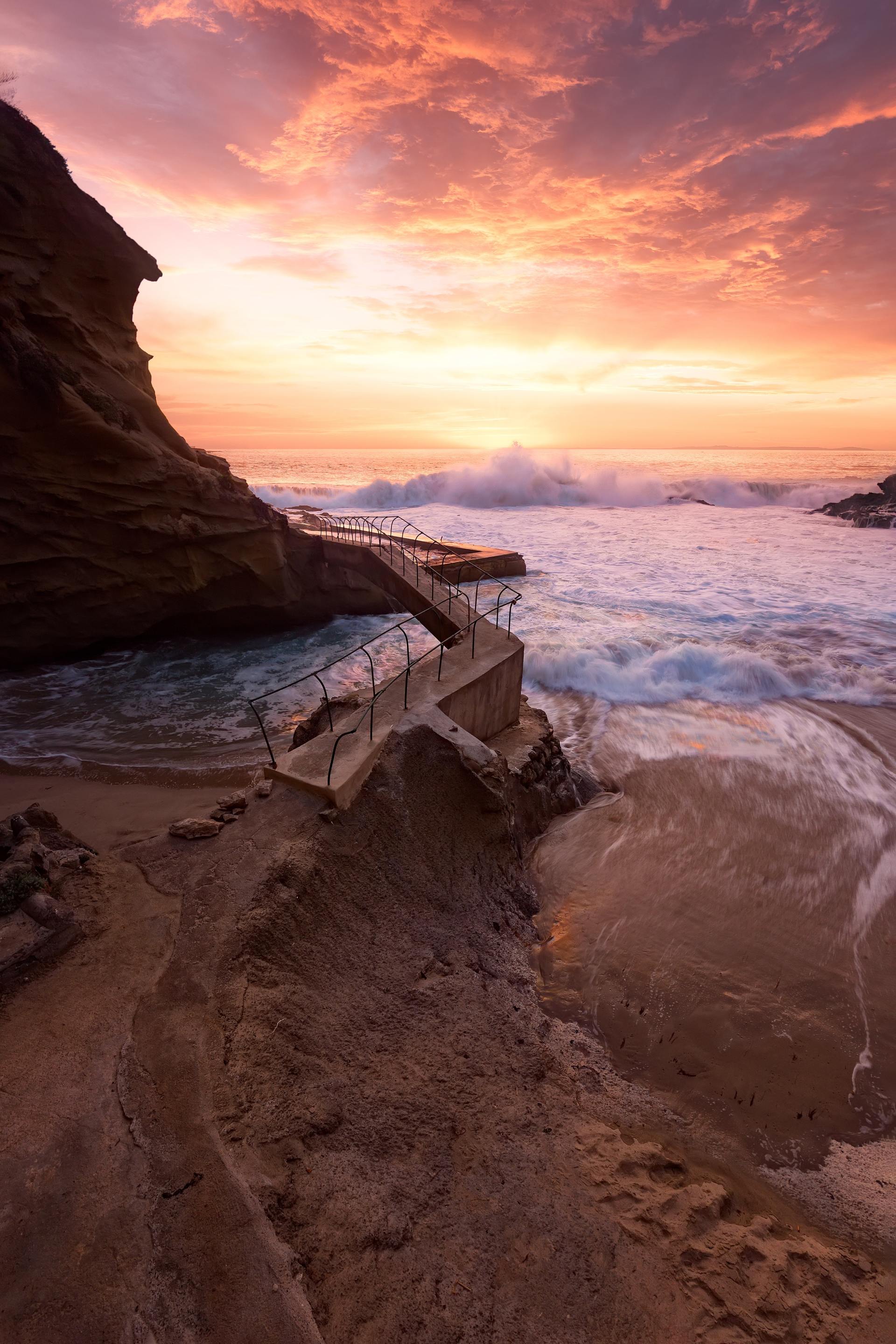 There is a staircase leading to the ocean at sunset.