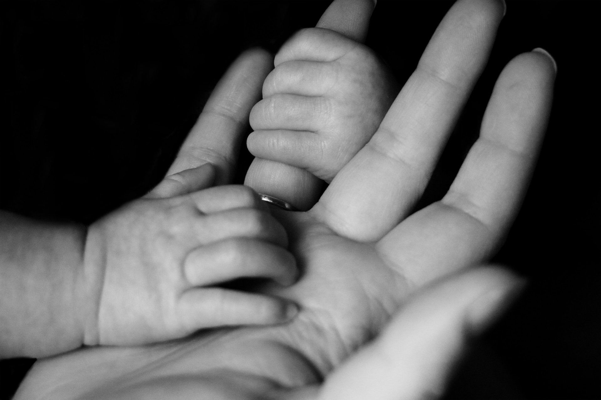 A black and white photo of a person holding a baby 's hand.