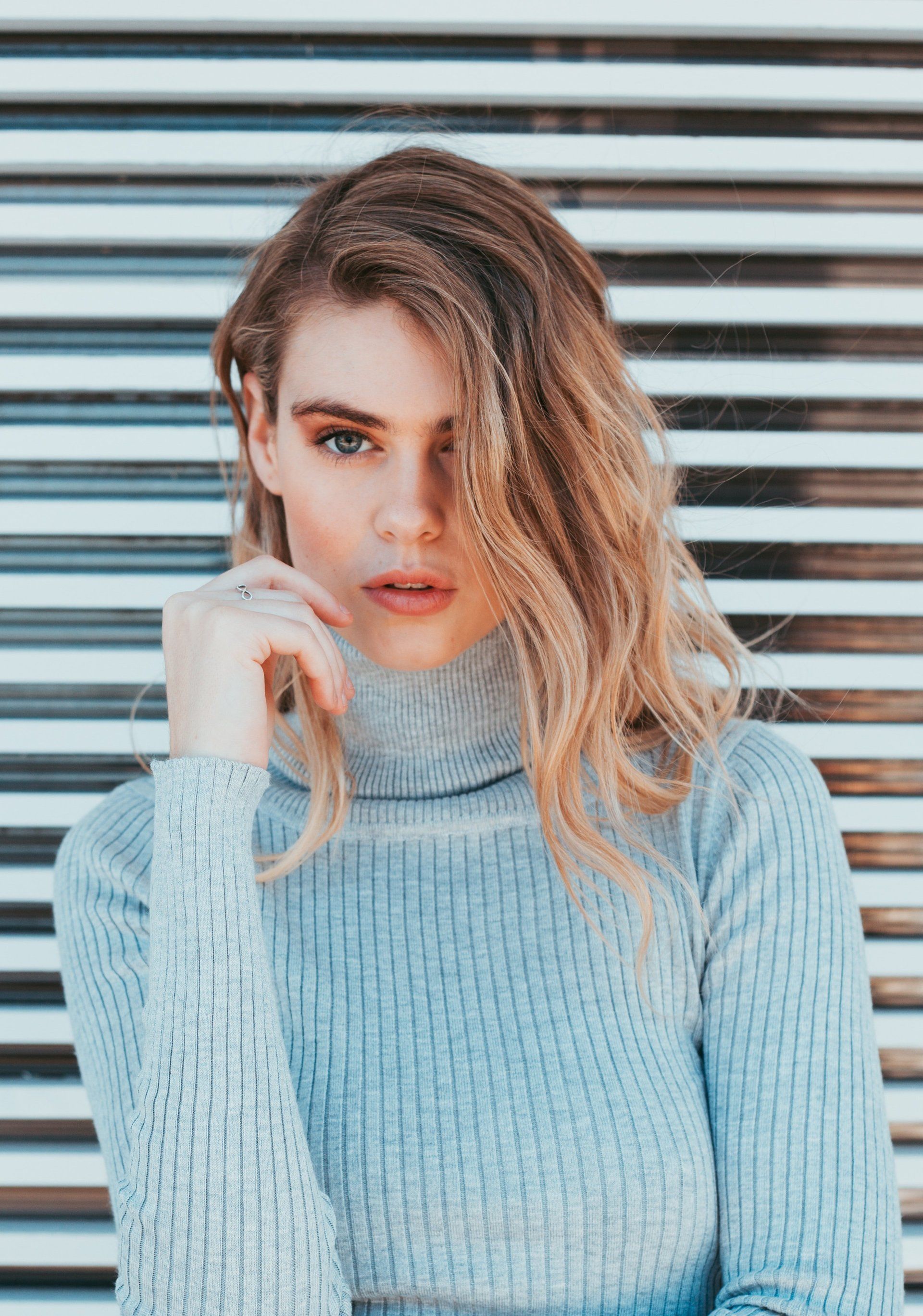 A woman wearing a turtleneck sweater is standing in front of a striped wall.