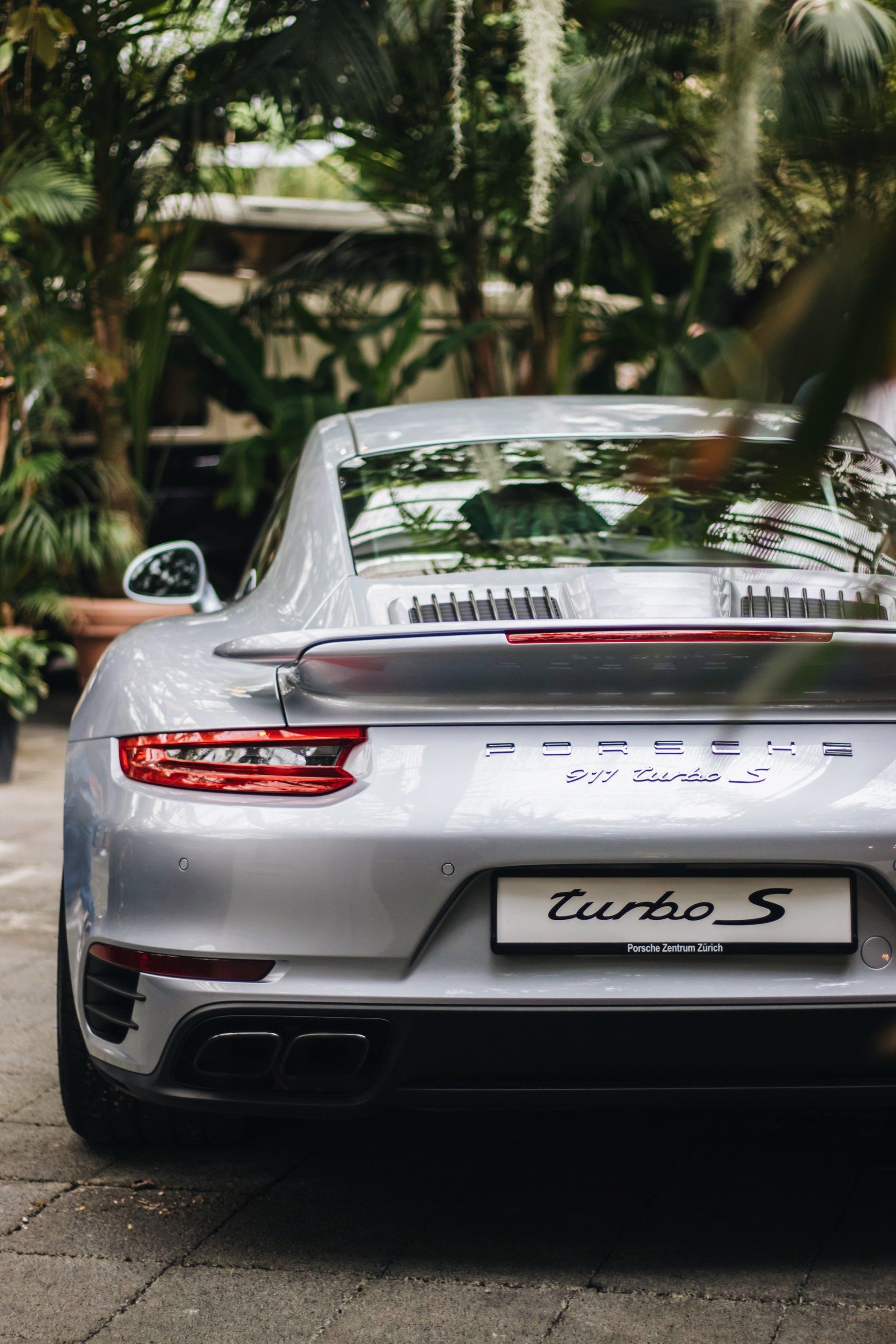 The rear end of a silver porsche turbo s is parked in a parking lot.