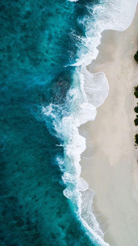 areal view of ocean hitting sand on beach