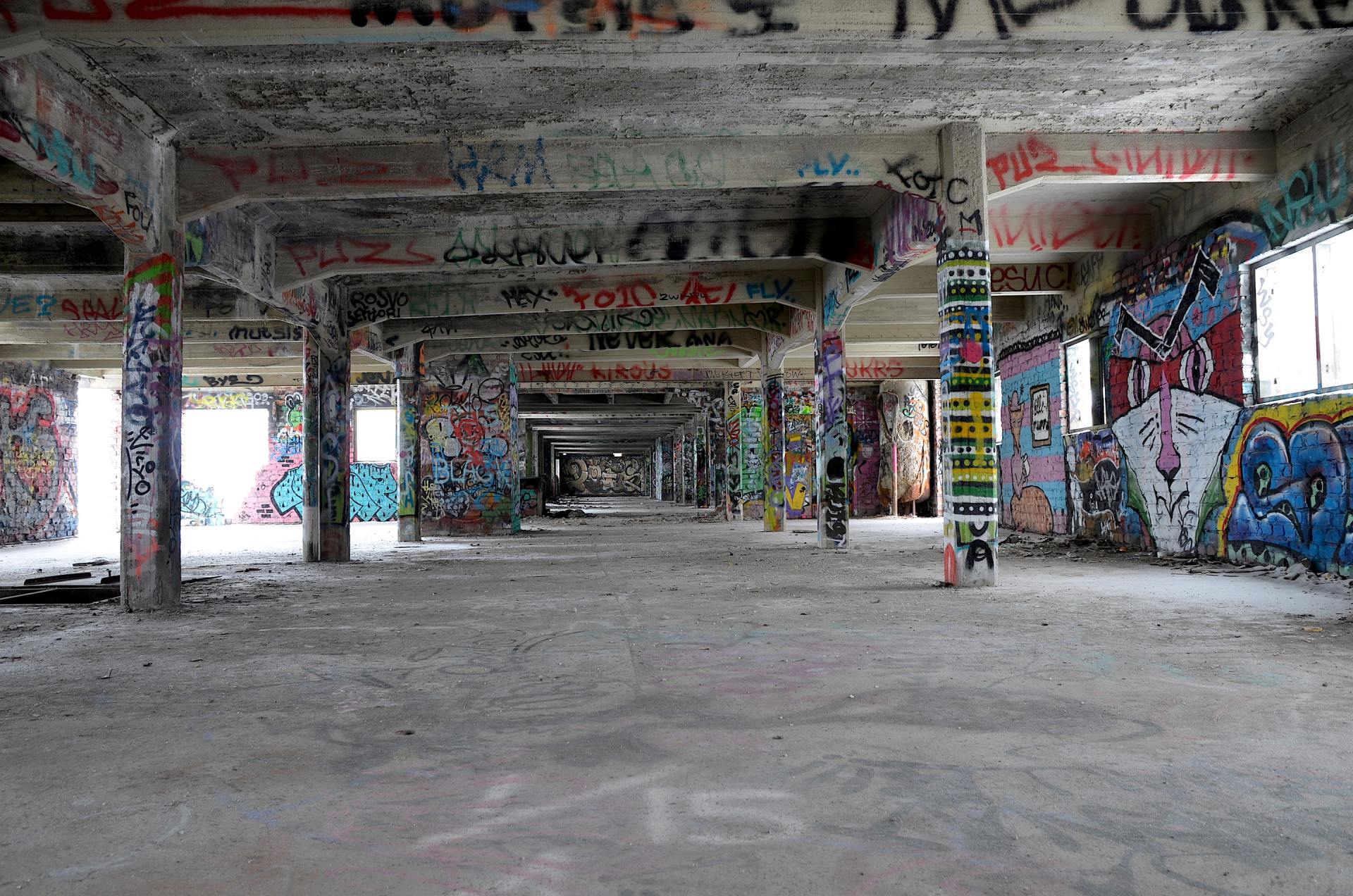 A large empty room with graffiti on the walls and columns.