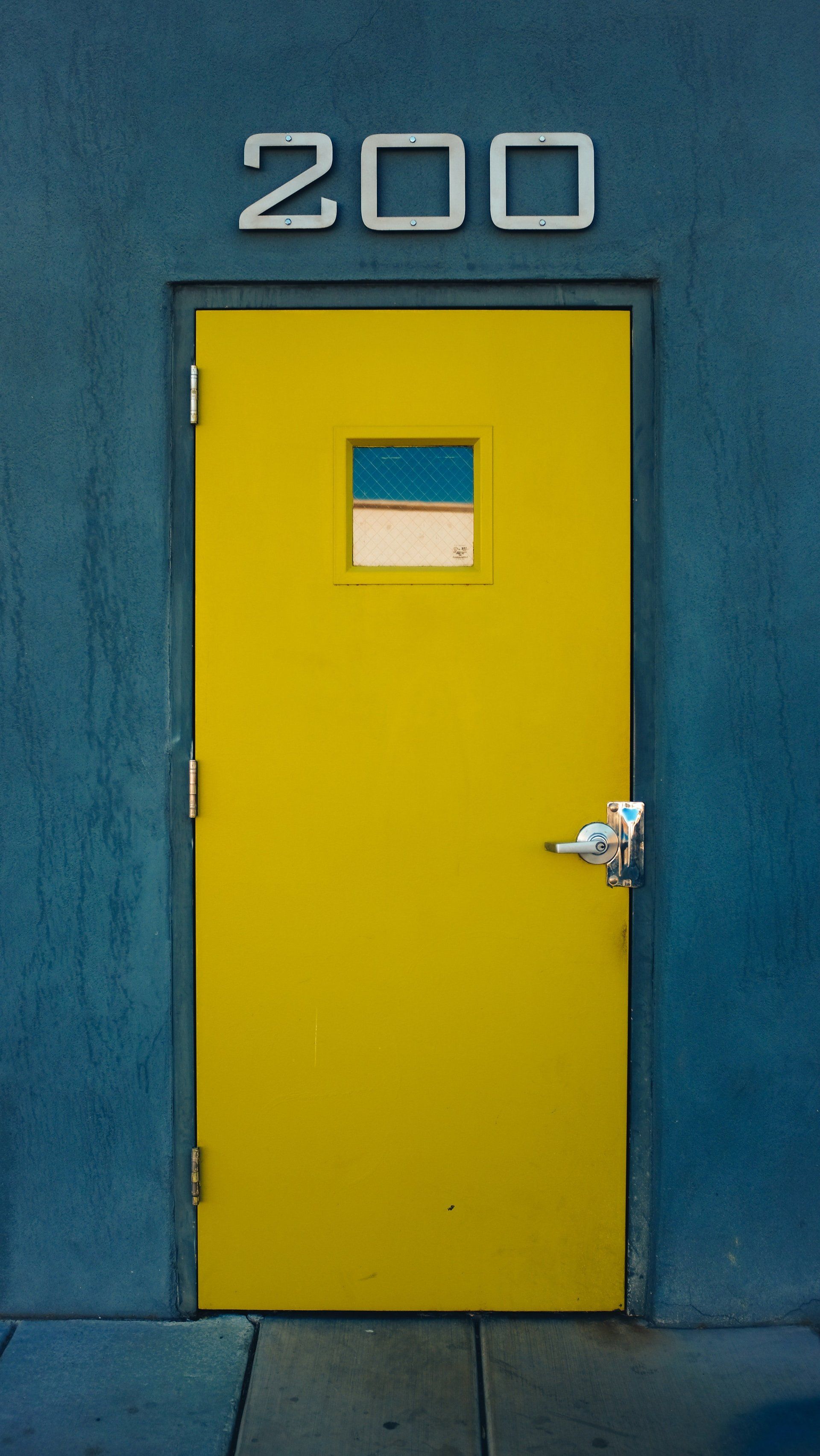Yellow door with a small window set in a blue wall; the number