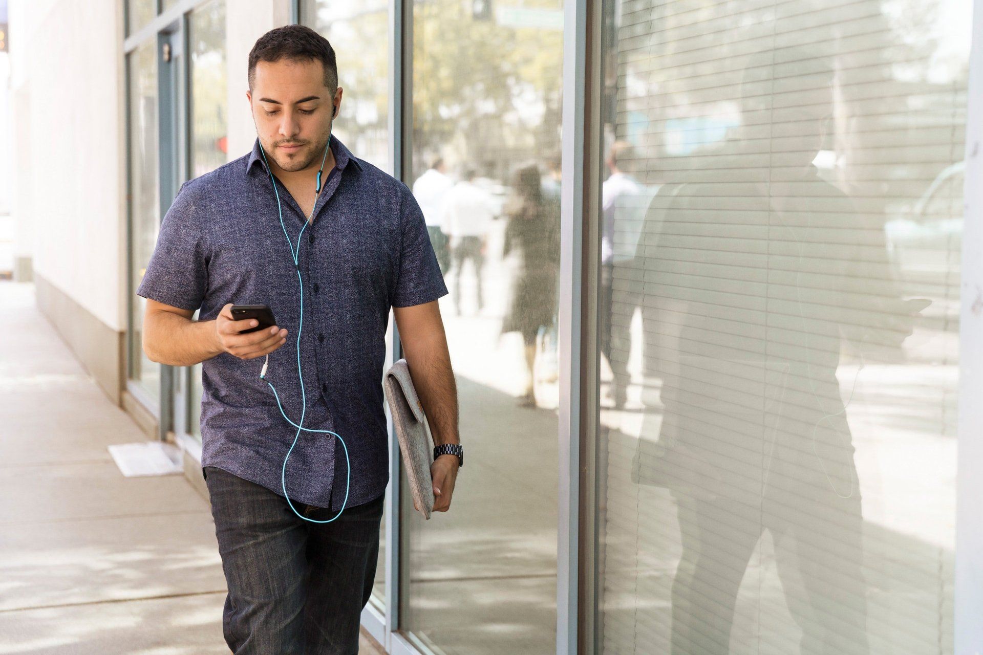 A man is walking down the street while listening to music on his phone.
