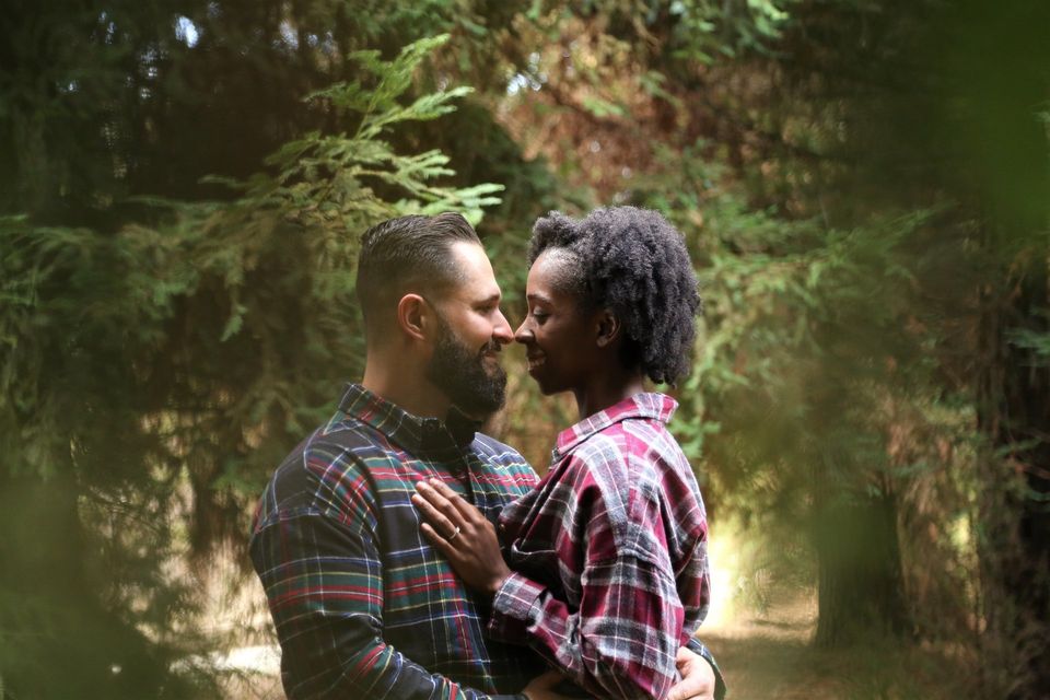 man and woman in woods close to each other appear in love she has wedding ring plaid shirts