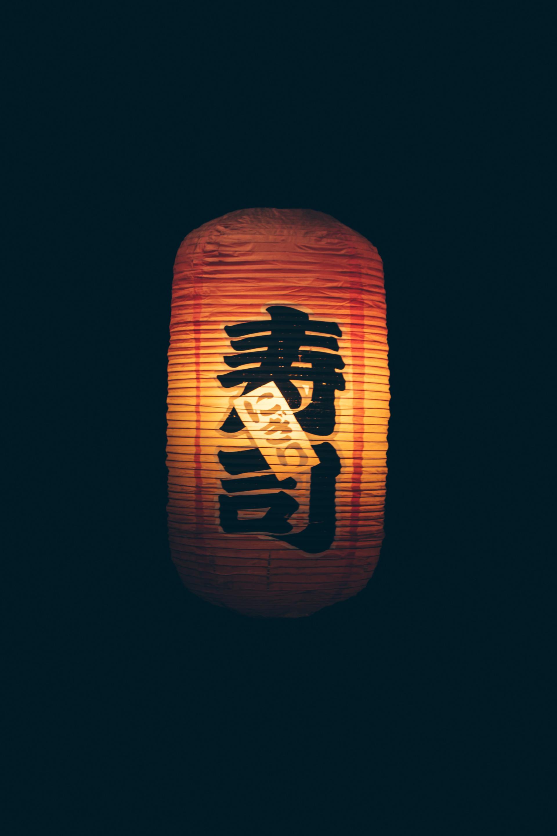 A lantern with chinese writing on it is lit up in the dark.