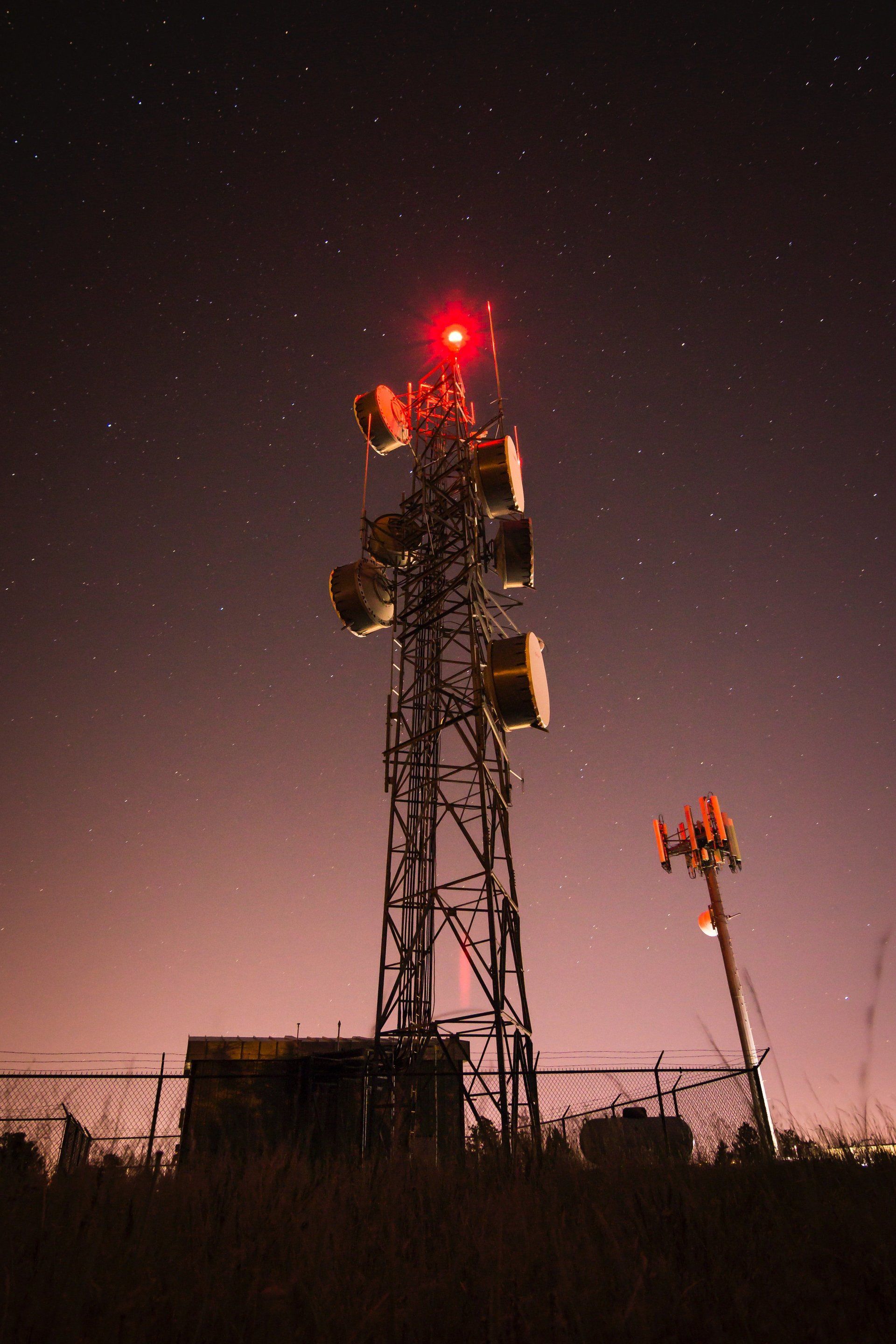 A telephone tower with a red light on top of it at night.