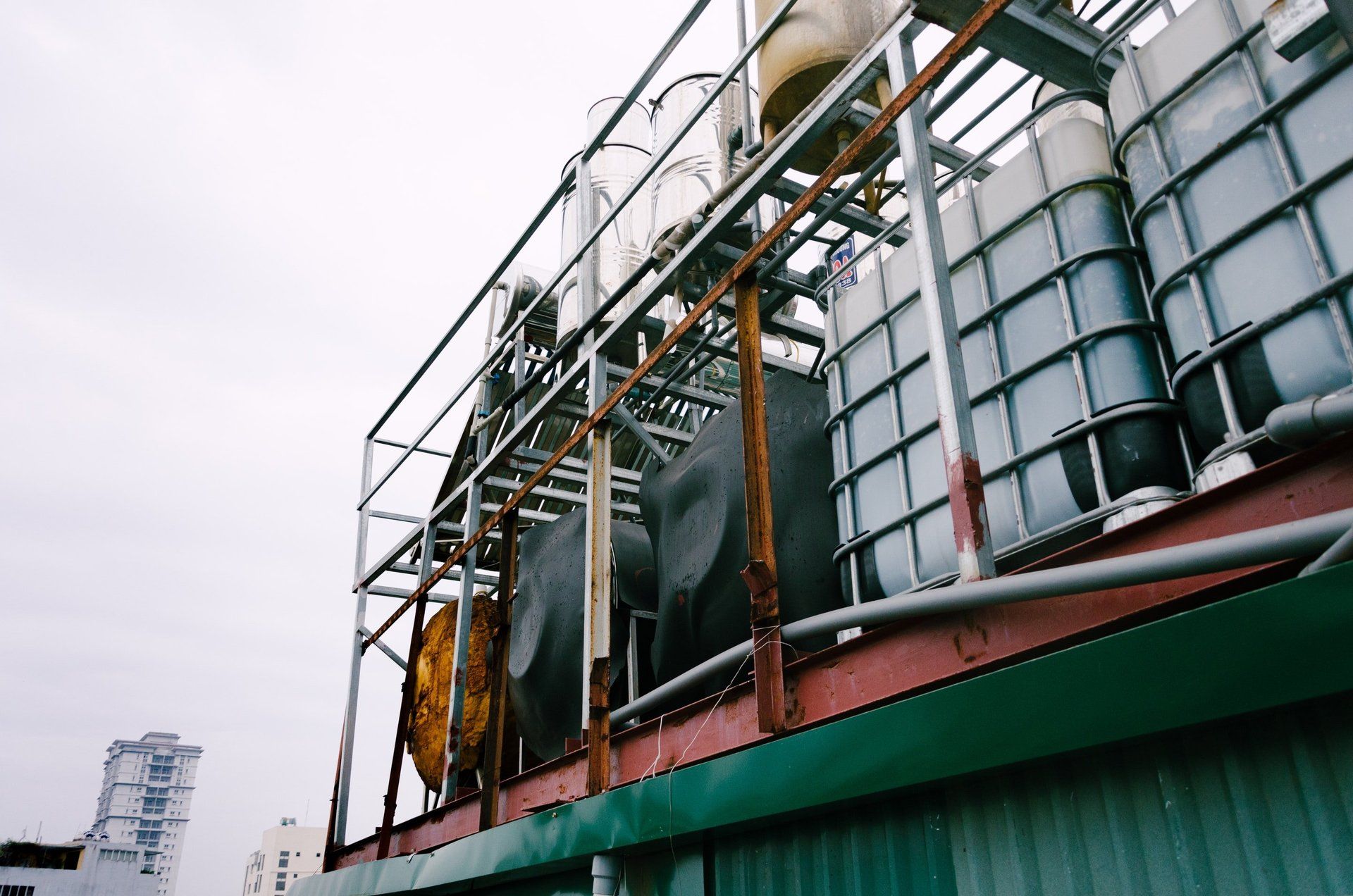 Metal tanks and pipes on a rooftop, supported by a rusty metal frame, cloudy sky.