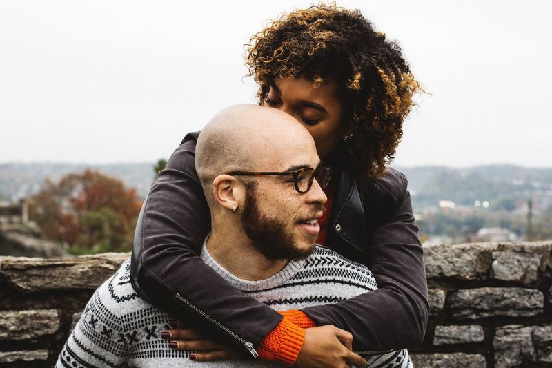 A man and a woman are hugging each other . the woman is kissing the man on the cheek.