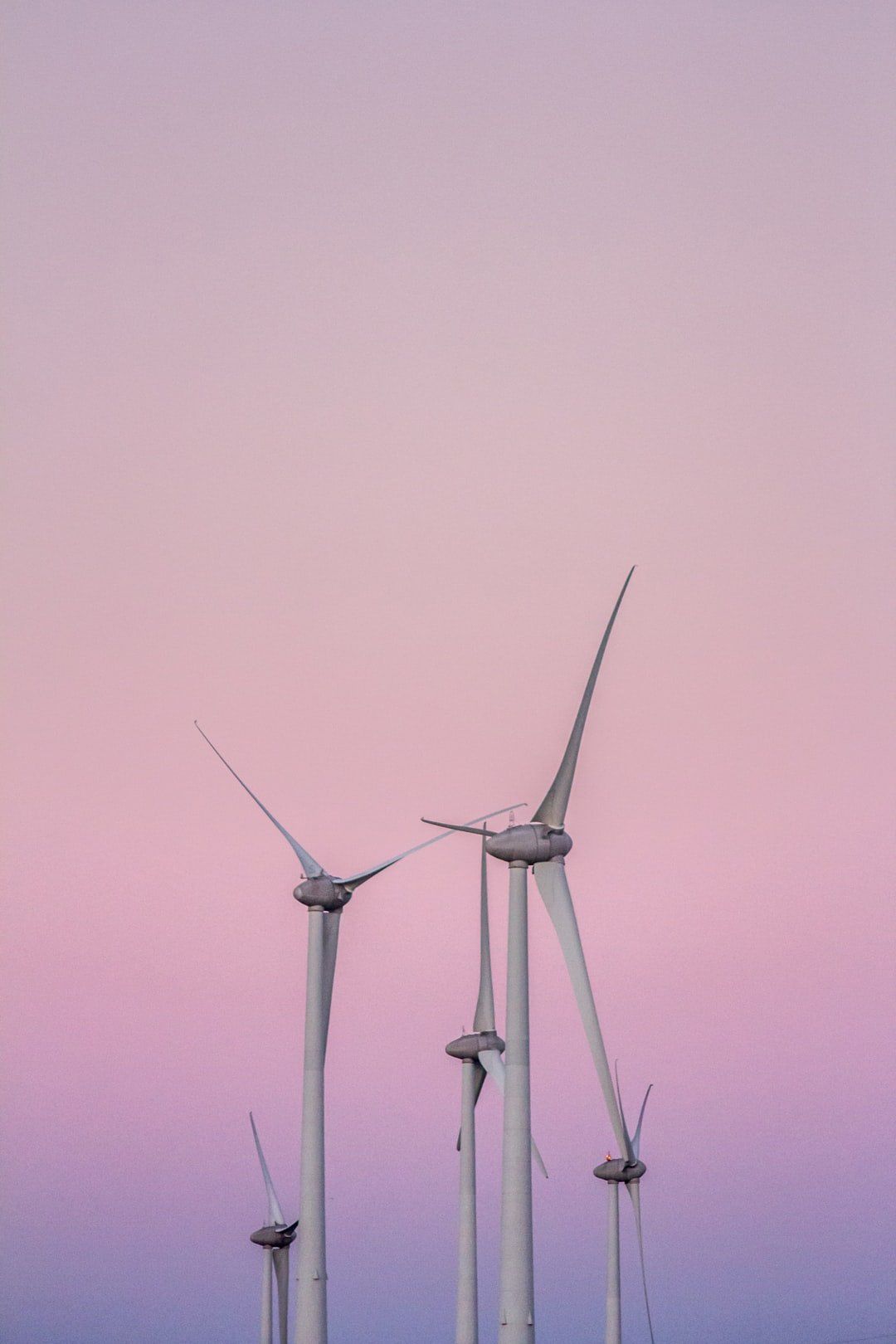 A row of wind turbines against a pink and purple sky at sunset.