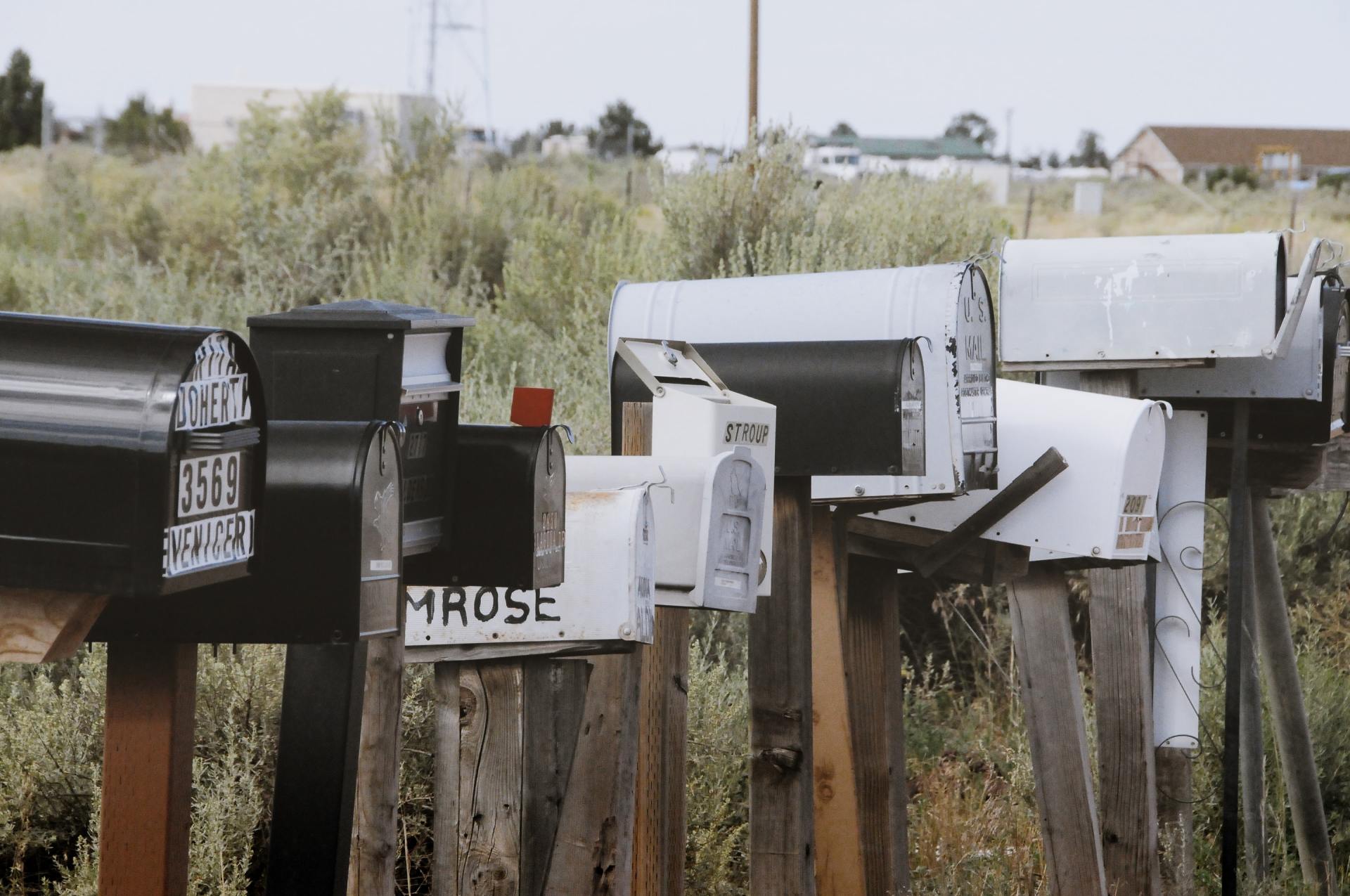 Row of mailboxes in front of dry grass, with buildings and a water tower in the distance.
